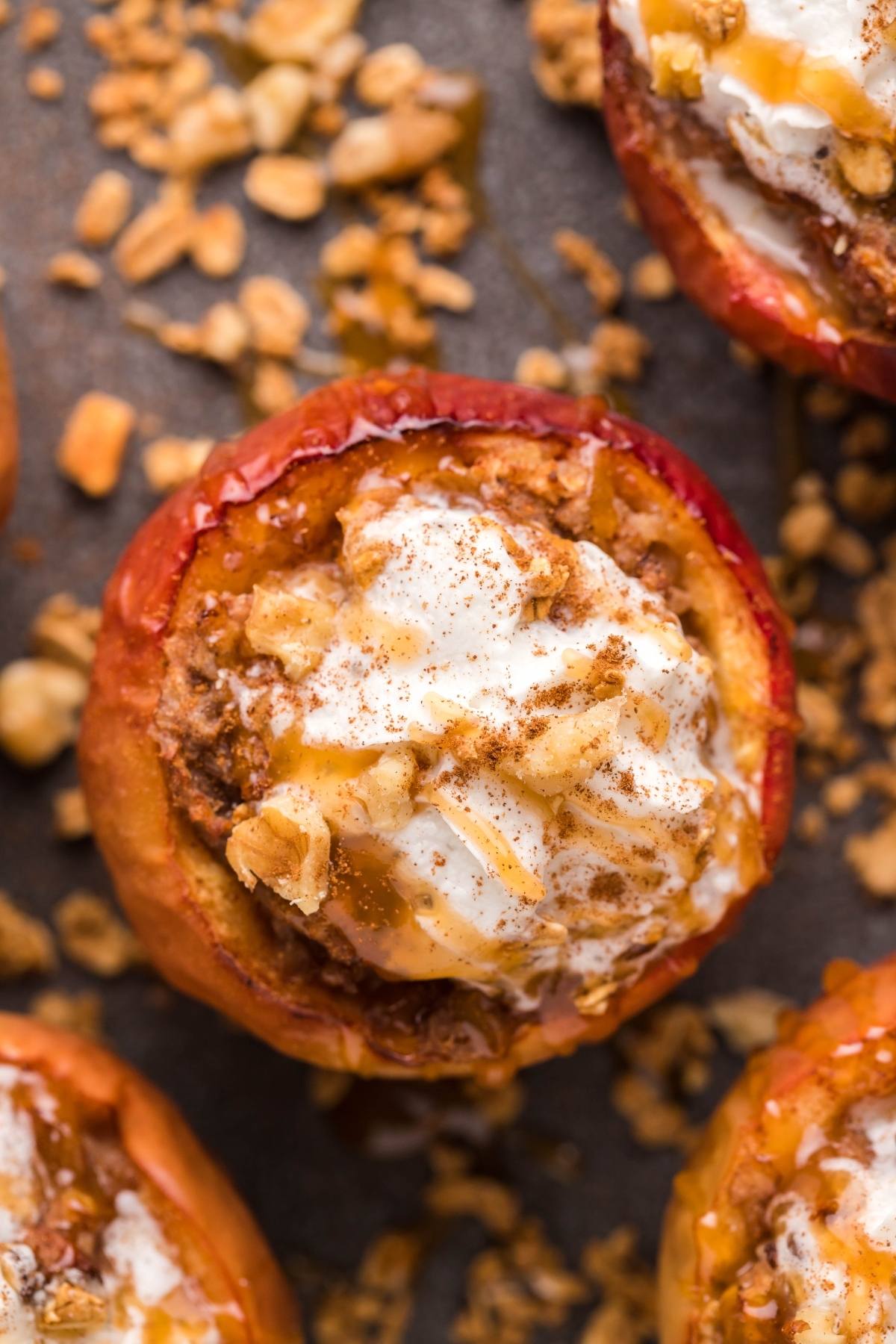 Air Fryer Baked Apples filled with oats and nuts, made with maple syrup, then topped with whipped cream and cinnamon on a dark surface.