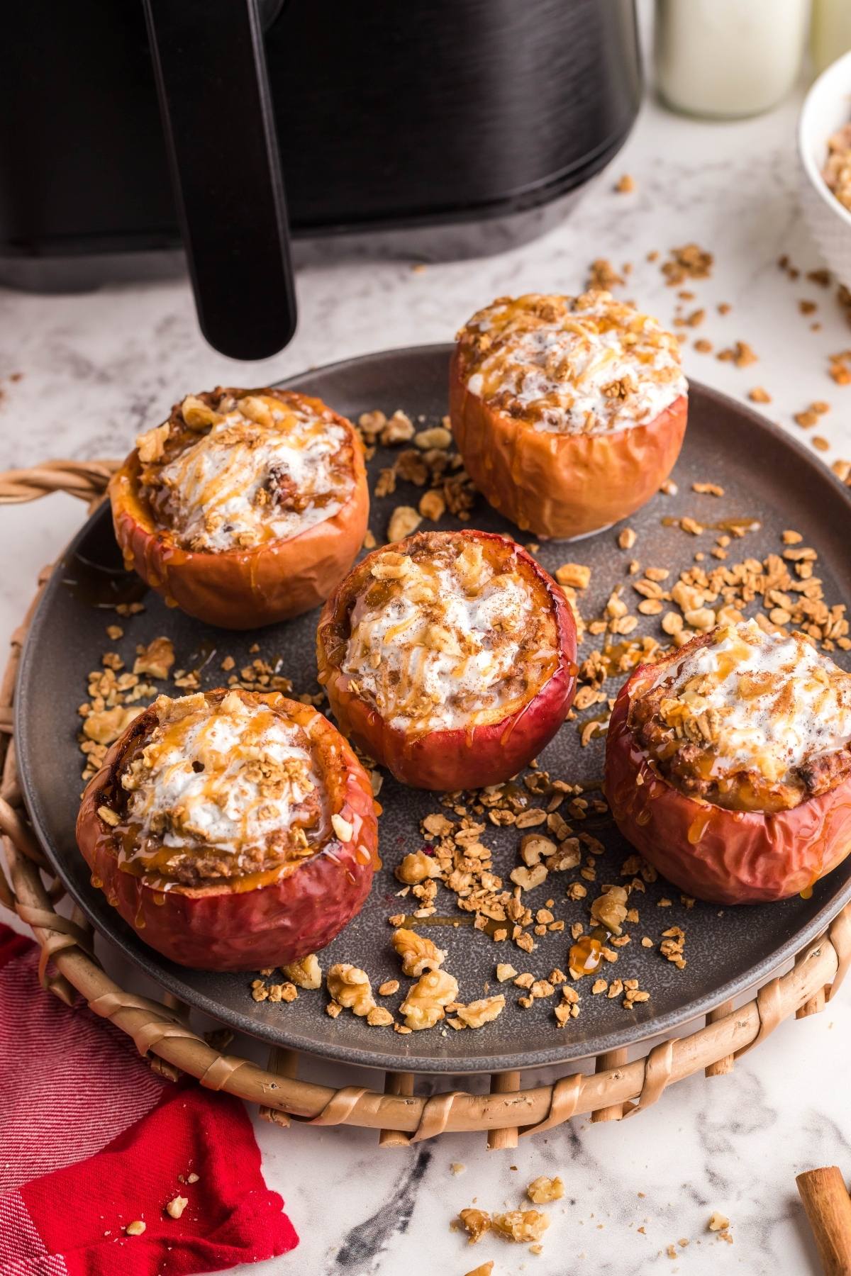 Air Fryer Baked Apples stuffed with oats and topped with melted cheese, made with maple syrup, served on a round plate near an air fryer.