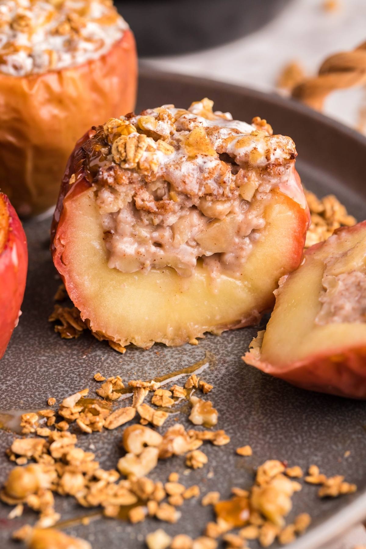 A baked apple stuffed with oats and nuts, cut in half on a plate, with granola scattered around—this Air Fryer Baked Apple is made with maple syrup for extra sweetness.