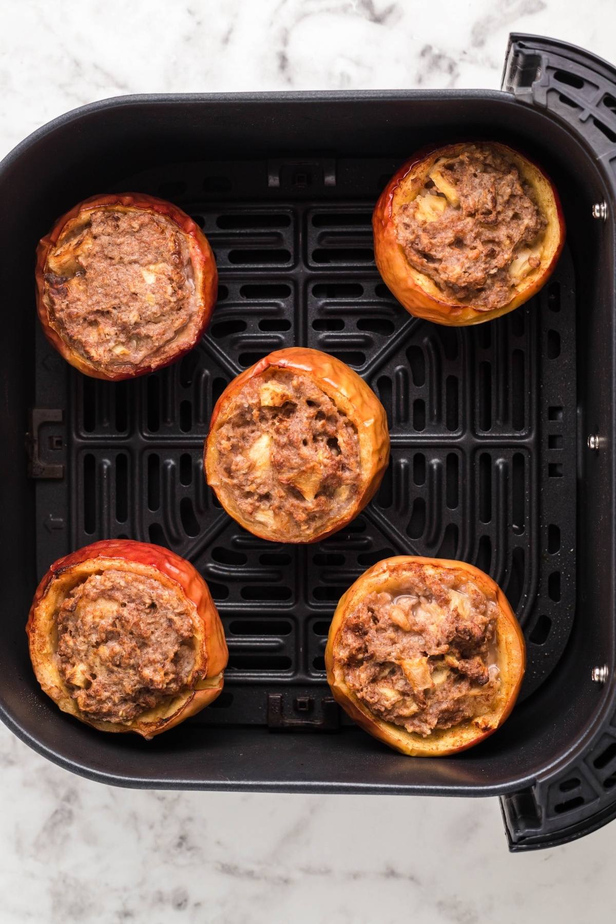 Five Air Fryer Baked Apples stuffed and ready in the basket, making a delightful air fryer apple dessert on a marble countertop.