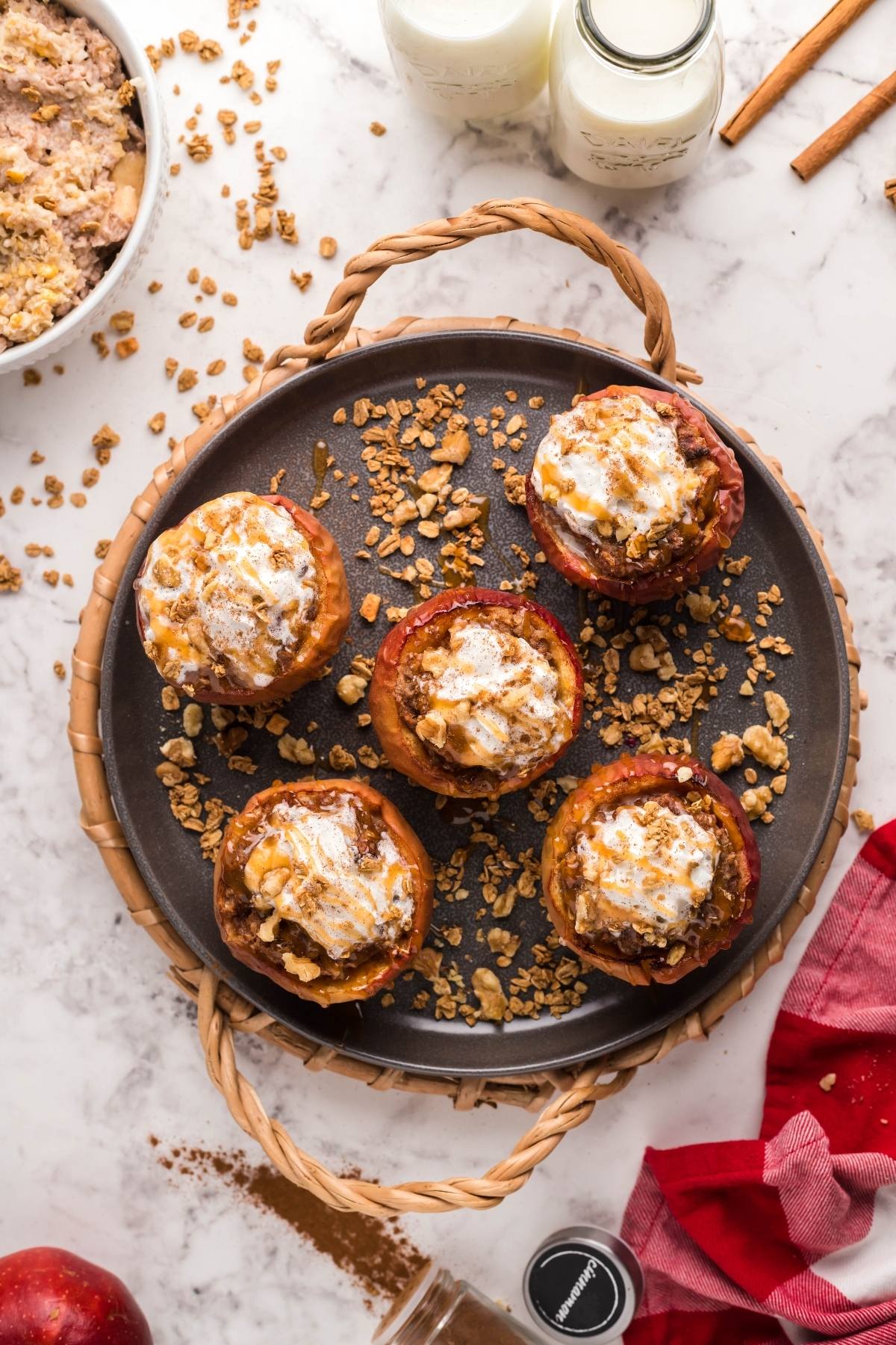 Five baked apples topped with oats and cream, served on a round plate with milk and spices beside—an easy air fryer apple dessert made with maple syrup for a cozy treat.