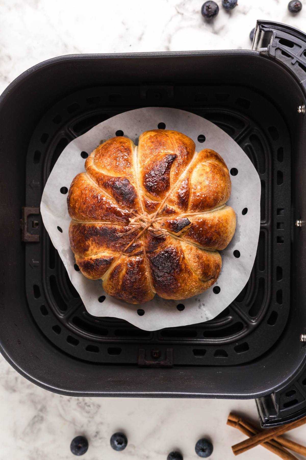 A golden brown round bread shaped like a flower sits on parchment inside an air fryer basket, perfect for baking in an air fryer and serving as a unique blueberry brie appetizer.