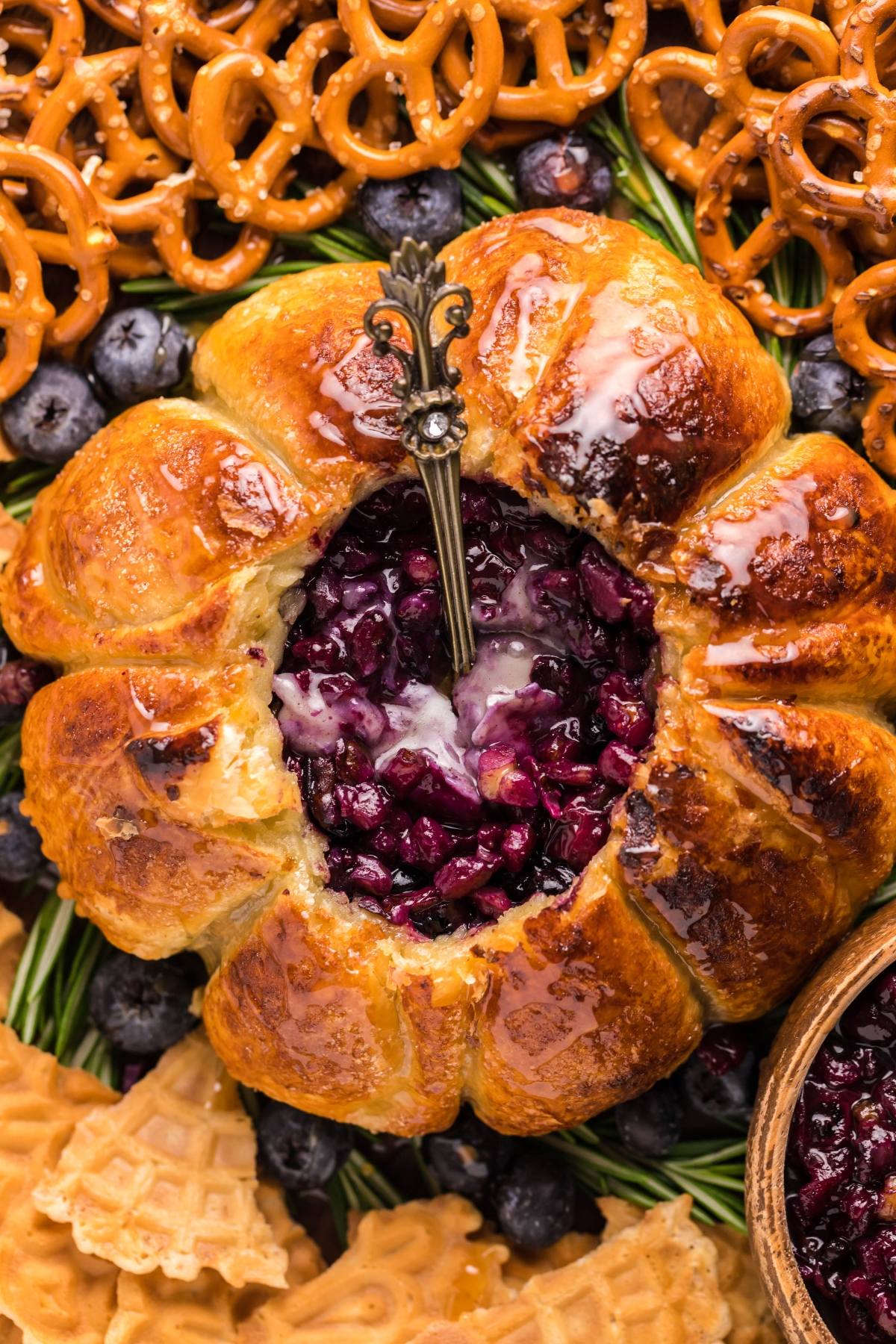 Air Fryer Baked Brie with Blueberries, filled with sweet berry preserves, is paired with pretzels, fresh blueberries, and waffle cookies—served warm and ready to enjoy with a spoon.