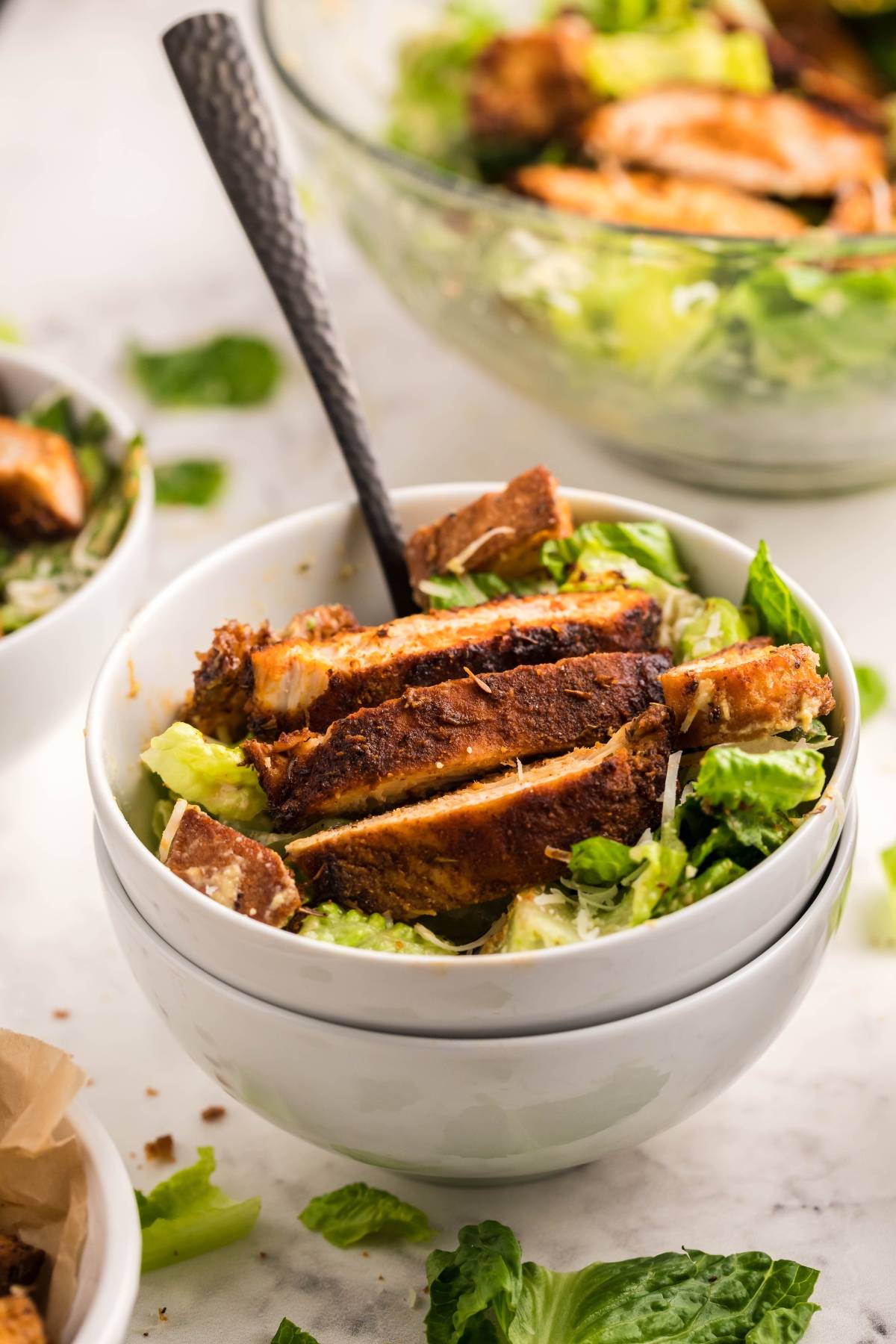 A bowl of Caesar salad topped with sliced Air Fryer Blackened Chicken, featuring the best homemade Caesar dressing, with a fork in the bowl.
