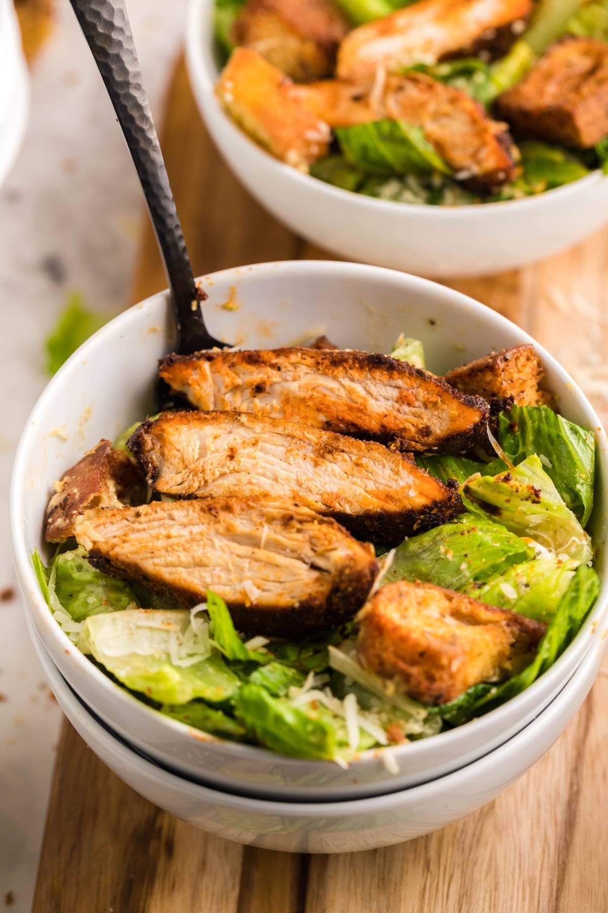 Bowl of Caesar salad topped with grilled chicken slices, air fryer homemade croutons, and grated parmesan cheese.