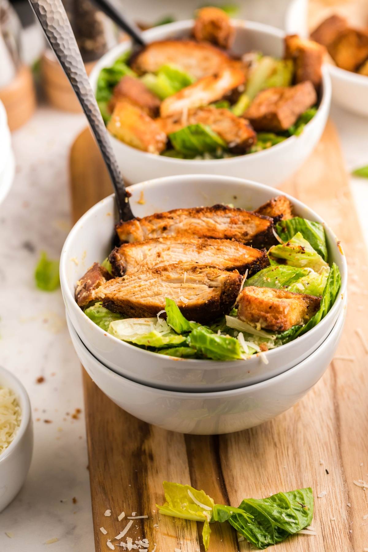 A bowl of Air Fryer Blackened Chicken Caesar Salad topped with sliced grilled chicken and croutons, placed on a wooden board. Enjoy with the best homemade Caesar dressing for extra flavor.