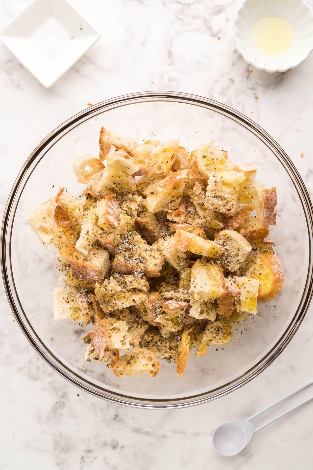 Cubed bread pieces tossed with herbs in a glass bowl on a marble countertop, perfect for air fryer homemade croutons to top salads with the best homemade Caesar dressing.