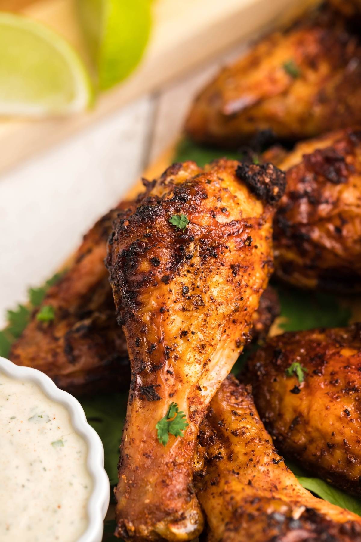 Close-up of seasoned, grilled chicken drumsticks garnished with herbs, served with a side of homemade firecracker ranch dressing for dipping.