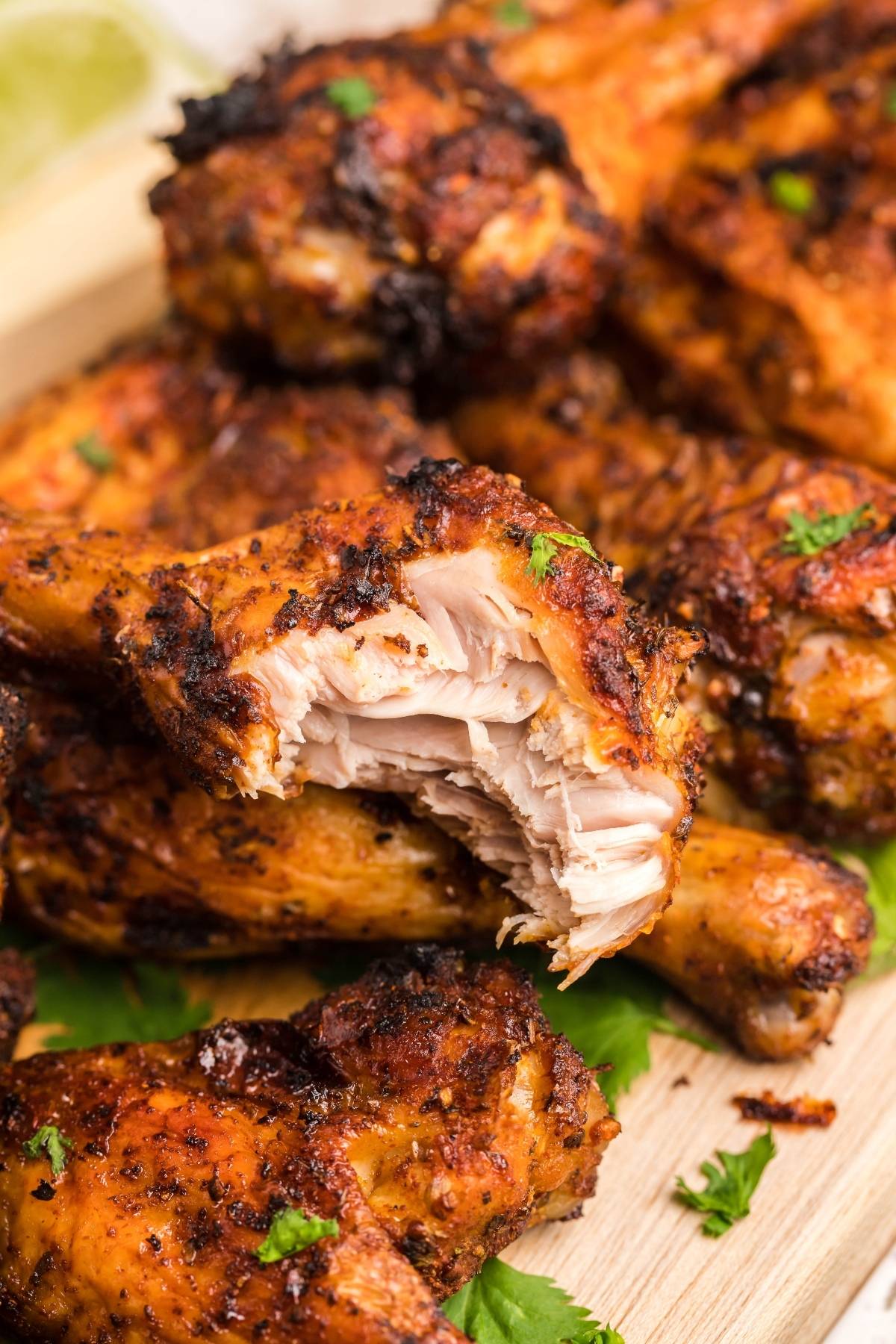 Grilled chicken drumsticks stacked on a wooden board, one with a bite taken, showing juicy, cooked meat inside—perfect for trying a Buttermilk firecracker ranch recipe.