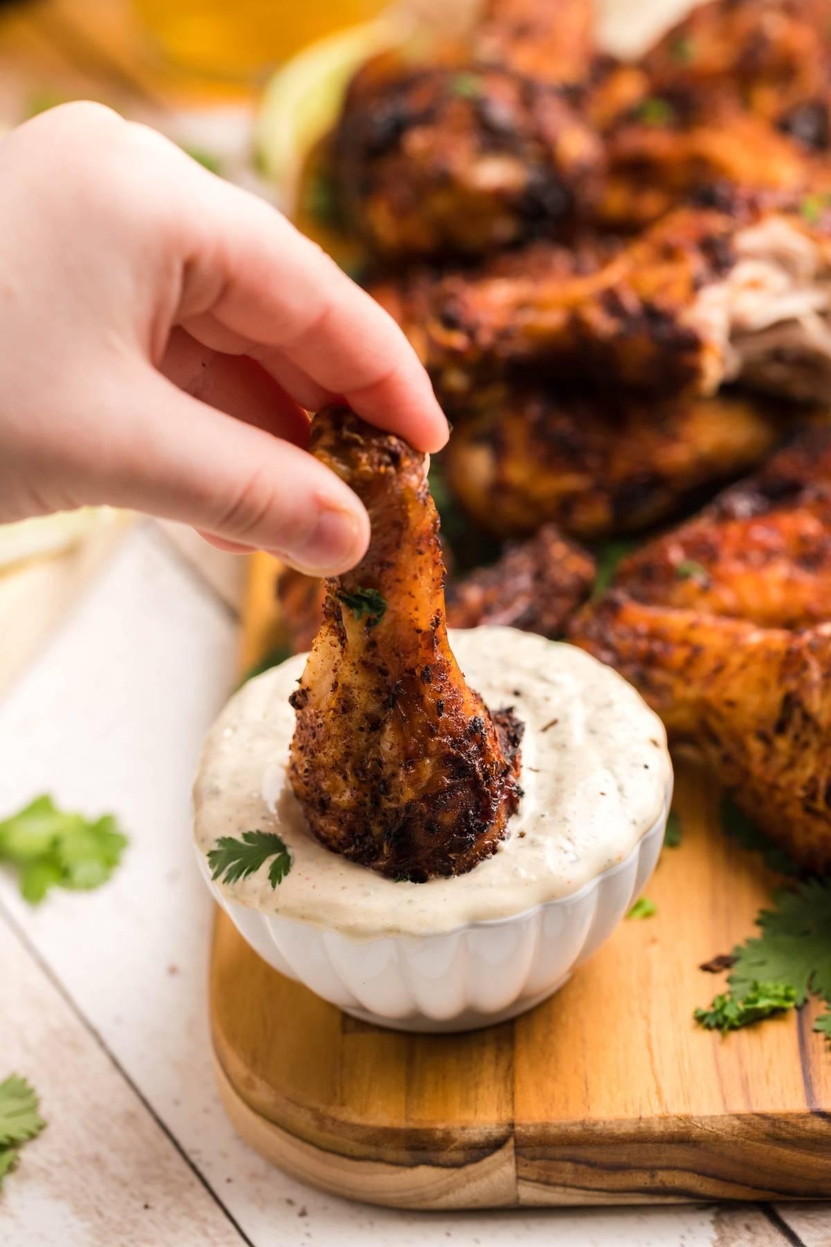 A hand dips a seasoned drumstick into a bowl of creamy white sauce, capturing the essence of Air Fryer Chipotle Chicken Wings paired with a zesty buttermilk firecracker ranch recipe.