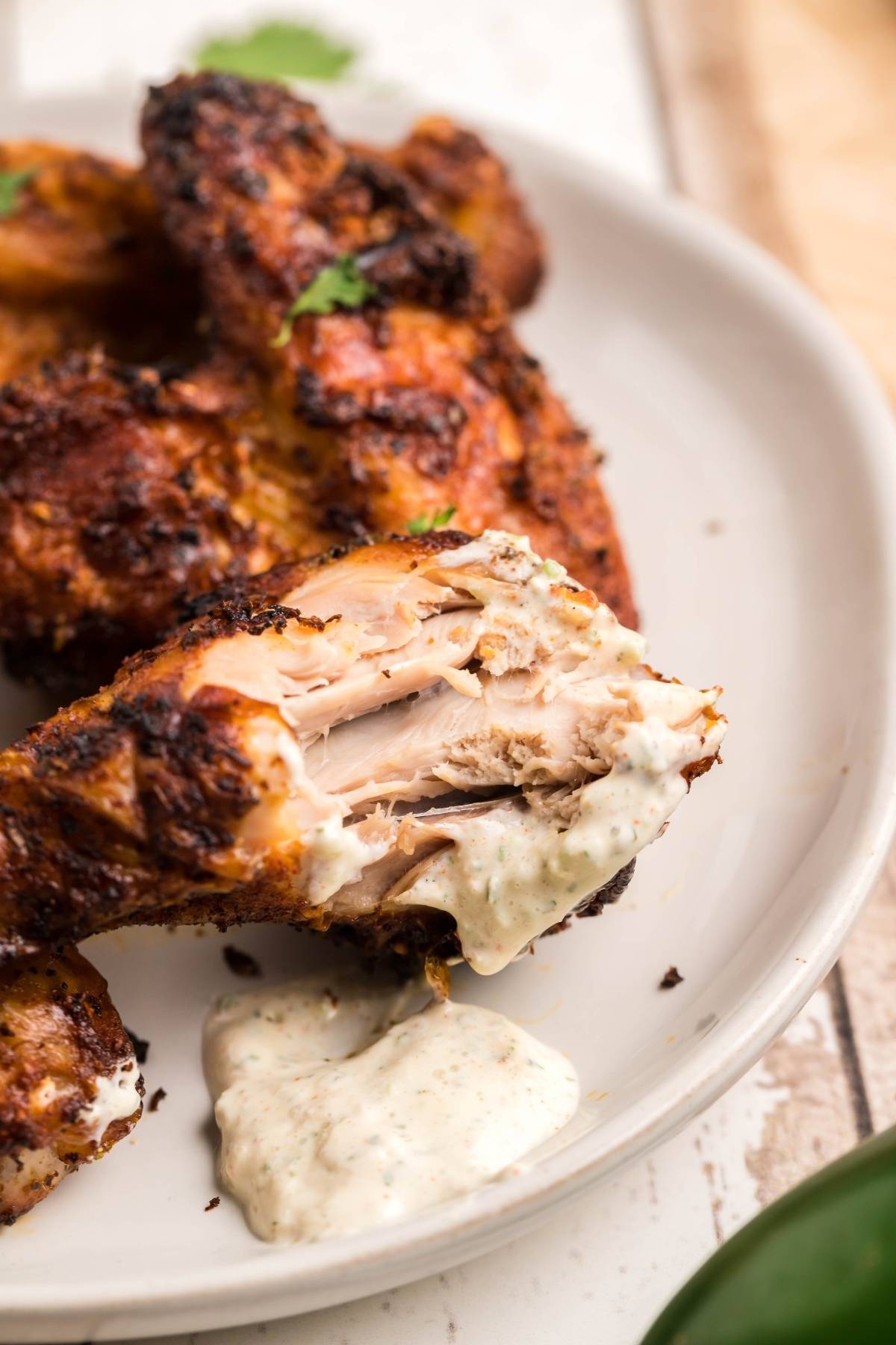 Grilled chicken drumstick with a bite taken out, dipped in creamy sauce on a white plate—a perfect match for any air fryer chicken recipe.