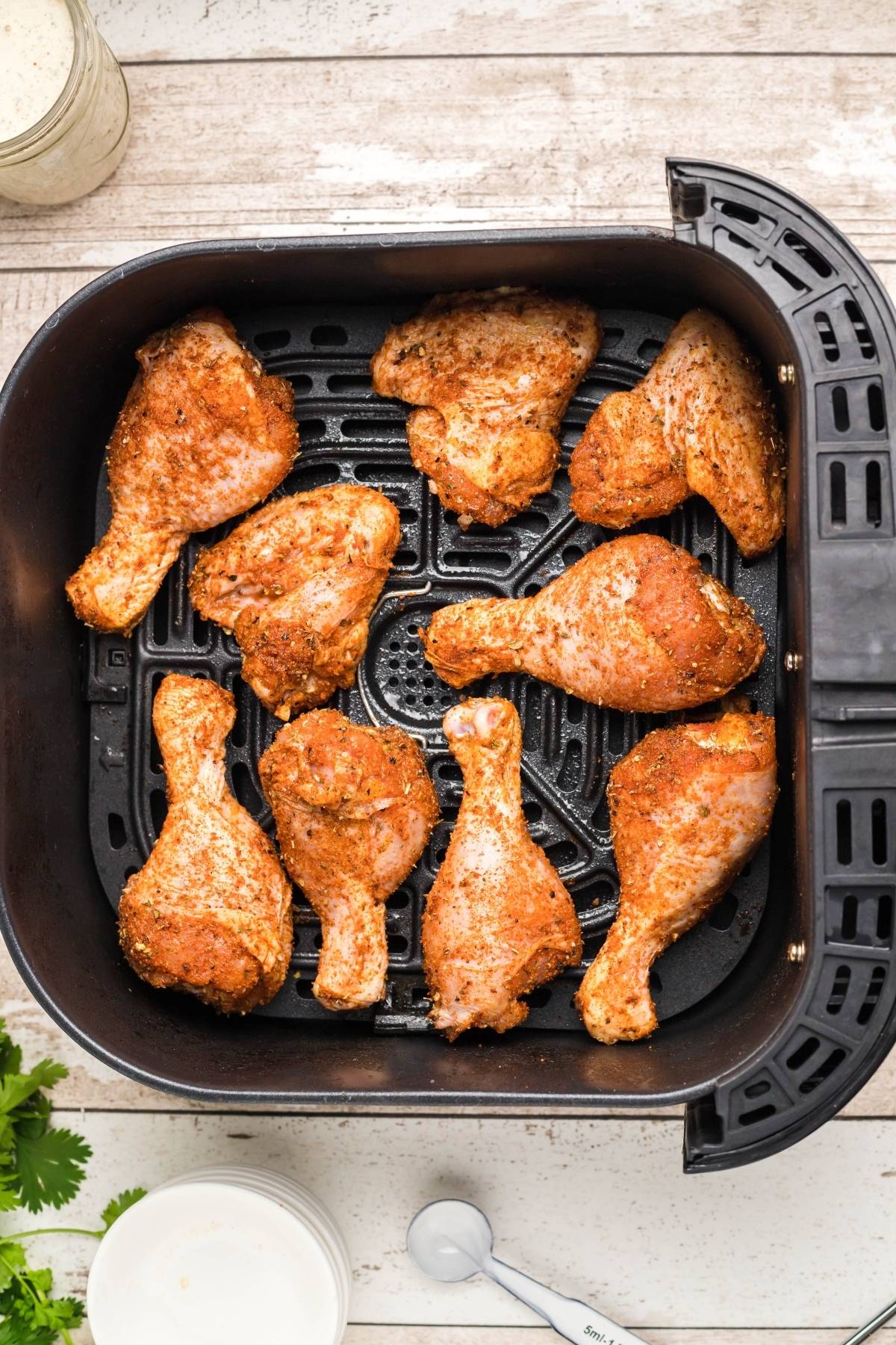 Seasoned chicken drumsticks arranged in a black air fryer basket, ready to be cooked using this easy air fryer chicken recipe. Perfect for pairing with homemade firecracker ranch dressing for an extra kick.