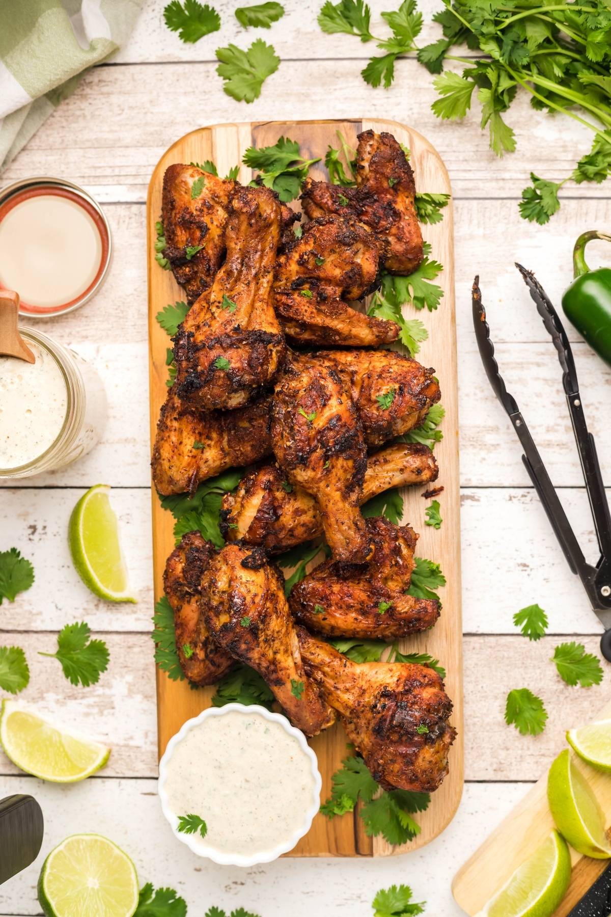 Grilled chicken wings on a wooden platter with cilantro, lime wedges, and dipping sauce—perfect inspiration if you're curious about how to make air fryer chicken wings at home.