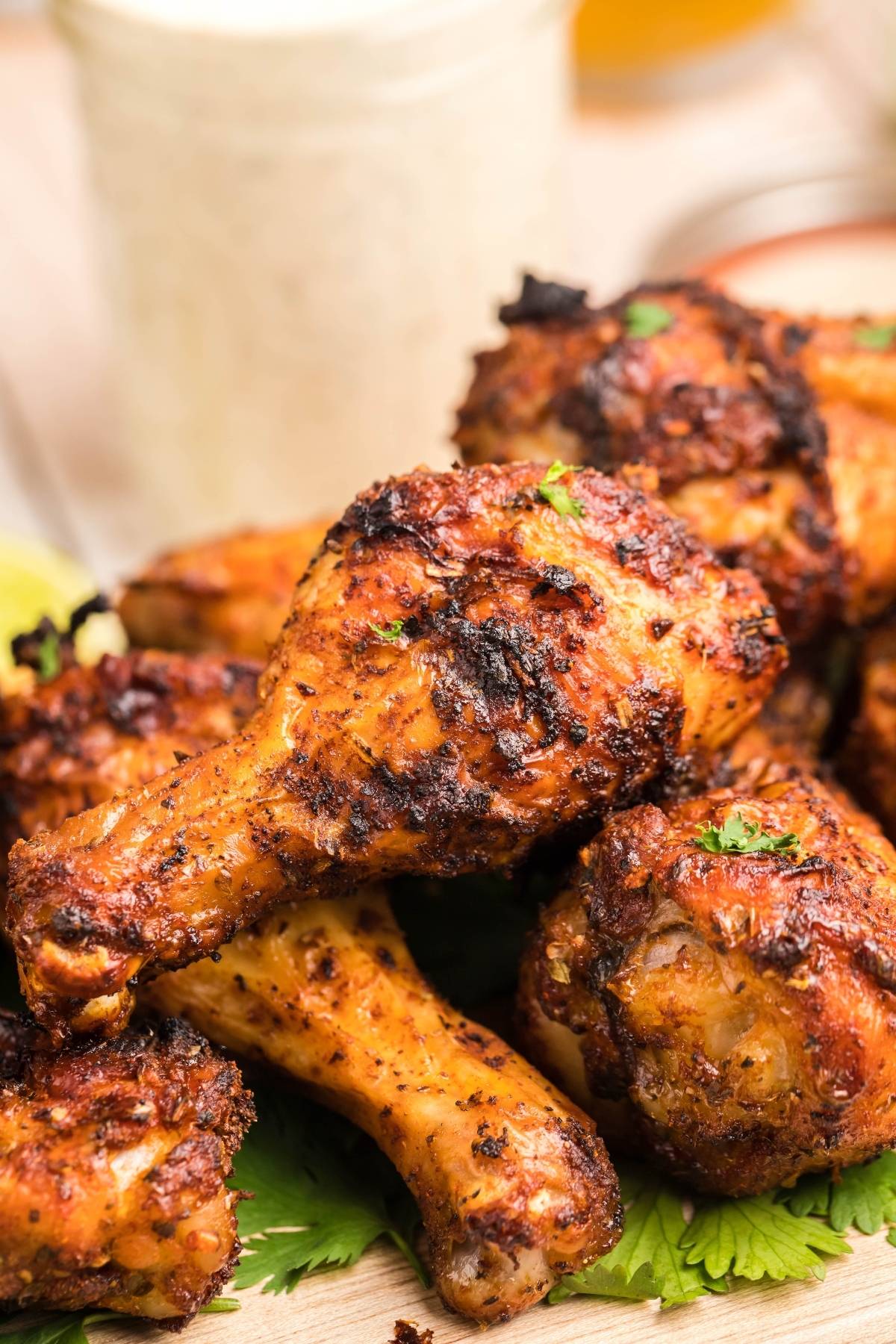 Close-up of crispy, seasoned grilled chicken drumsticks piled on a plate with herbs, served alongside homemade firecracker ranch dressing for the perfect flavorful dip.