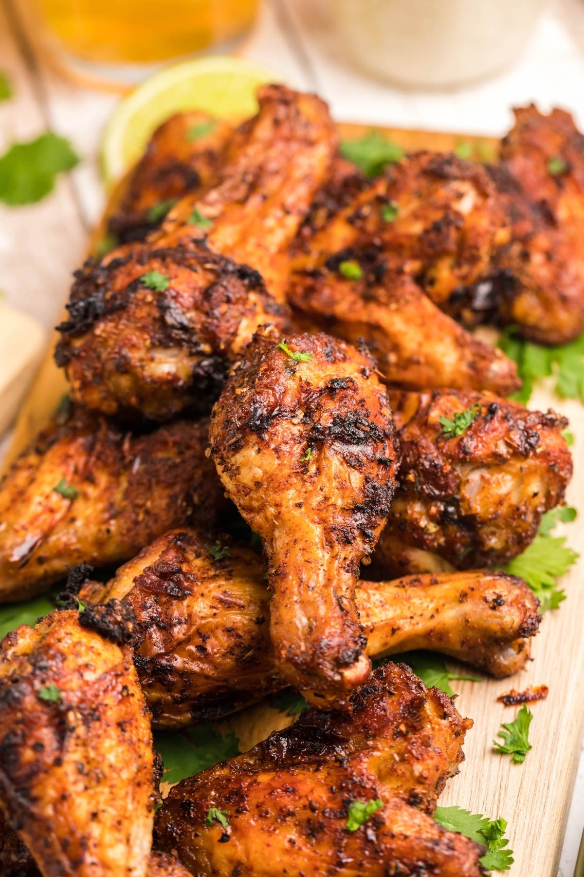 Grilled, seasoned chicken drumsticks and wings are stacked on a wooden board with green herbs sprinkled on top—perfect inspiration if you're searching for an easy air fryer chicken recipe.