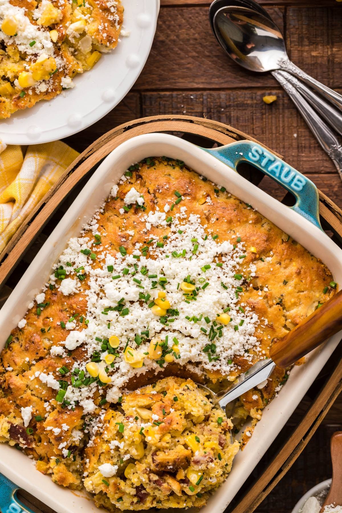 Baked Mexican street corn casserole, made with Jiffy cornbread mix and topped with cheese and herbs, served in a blue Staub dish with a spoon.