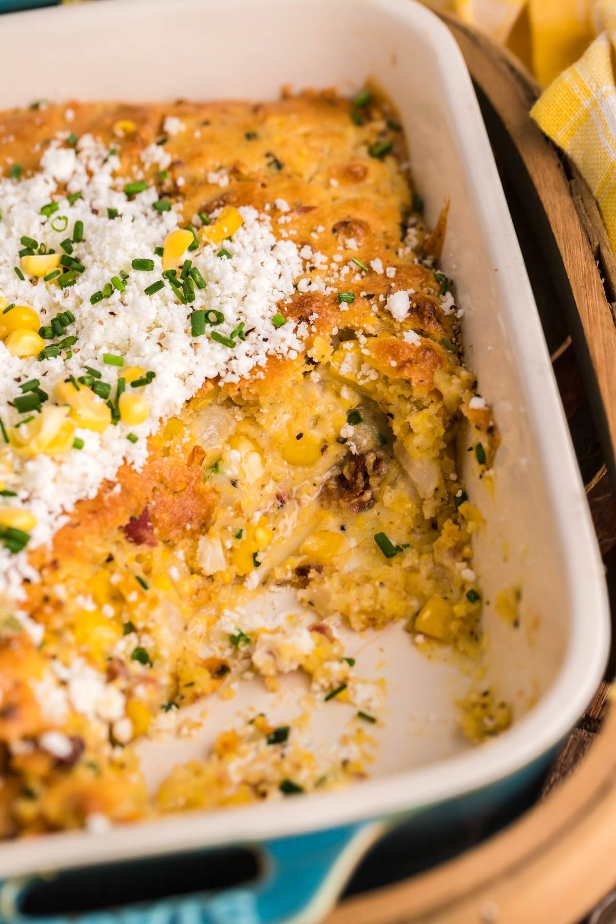 Bacon corn casserole made with Jiffy cornbread mix, topped with cheese, chives, and crumbled bacon, with a serving scooped out from the dish.