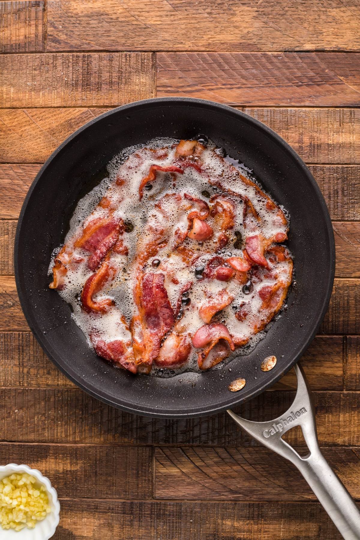 Sizzling bacon strips cooking in a black skillet on a wooden countertop—the perfect start for bacon corn casserole made with Jiffy cornbread mix.
