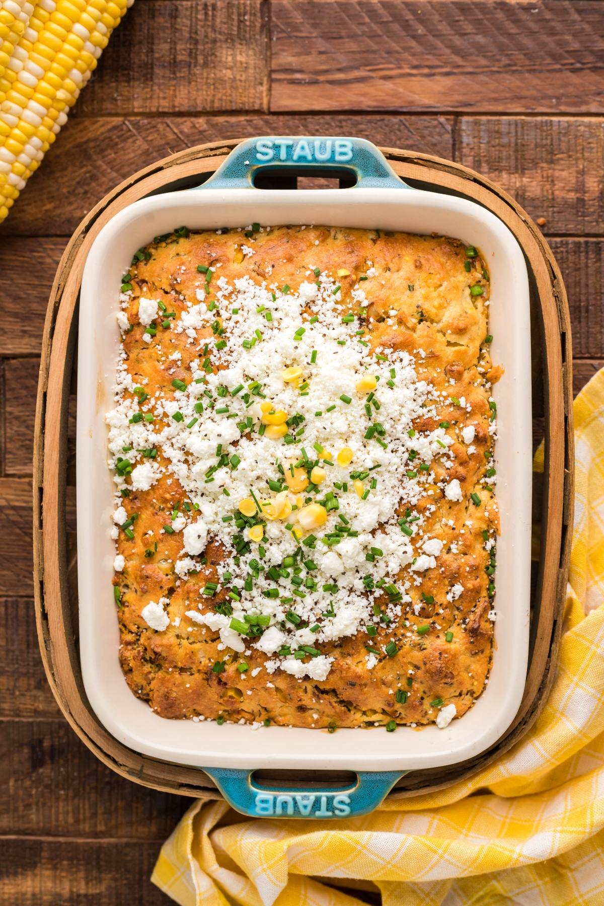 Baked cornbread topped with crumbled cheese, chives, and corn in a blue-handled dish on a wooden table—perfect for serving as the best corn casserole.