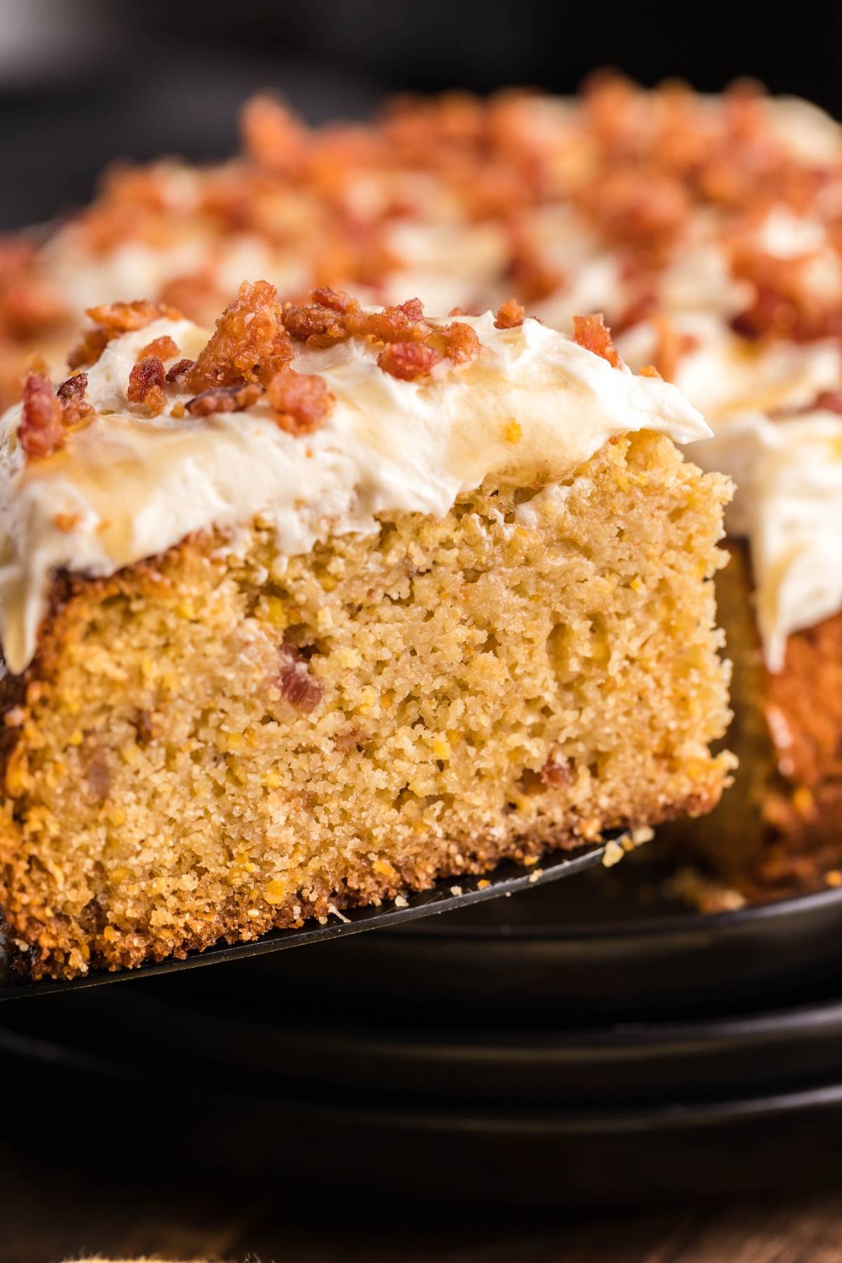 A slice of moist sweet cornbread with icing, topped with white frosting and bacon crumbles, creates a unique cornbread dessert.