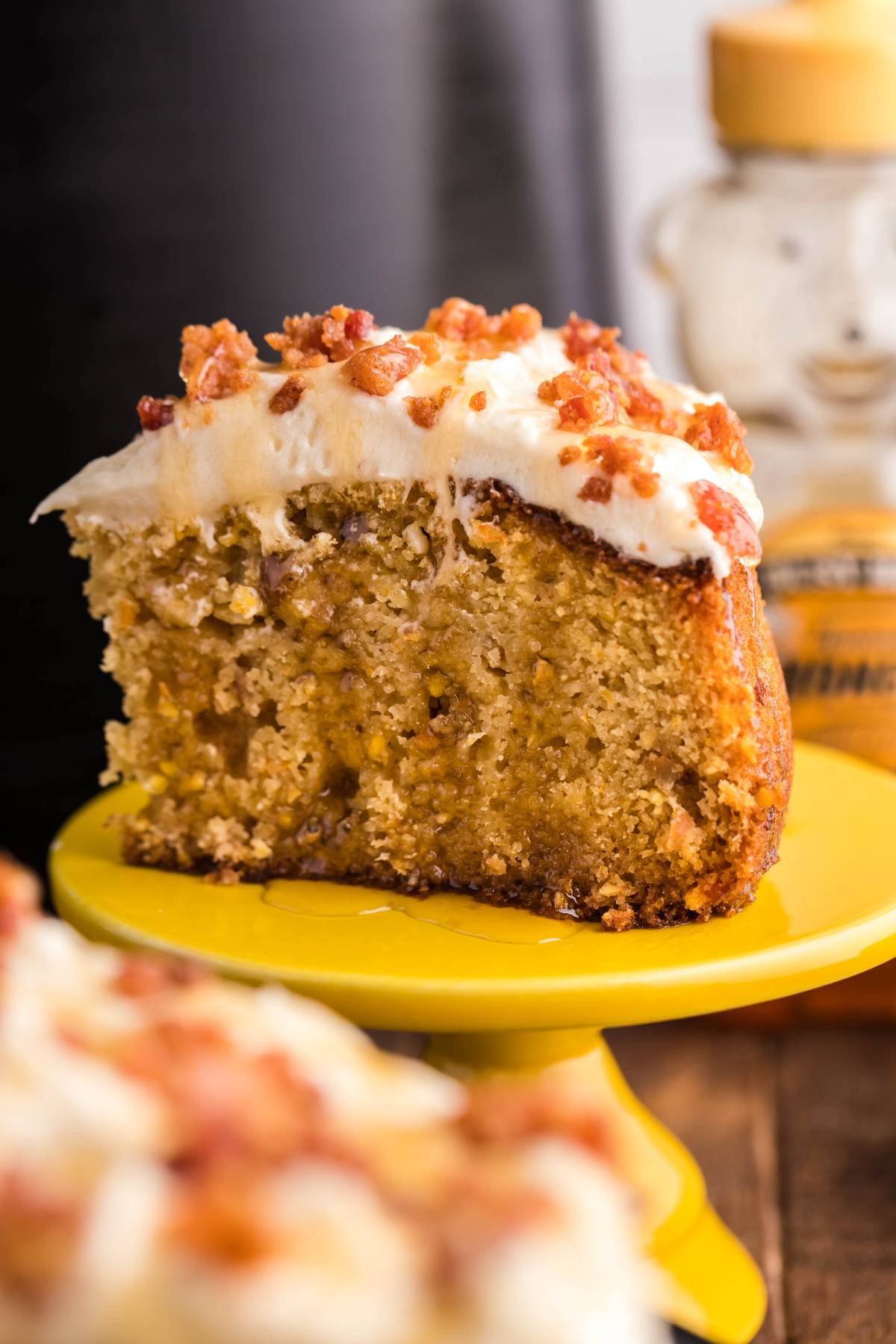 A slice of Air Fryer Cornbread Cake with Honey Buttercream and bacon bits on top, served on a yellow plate.