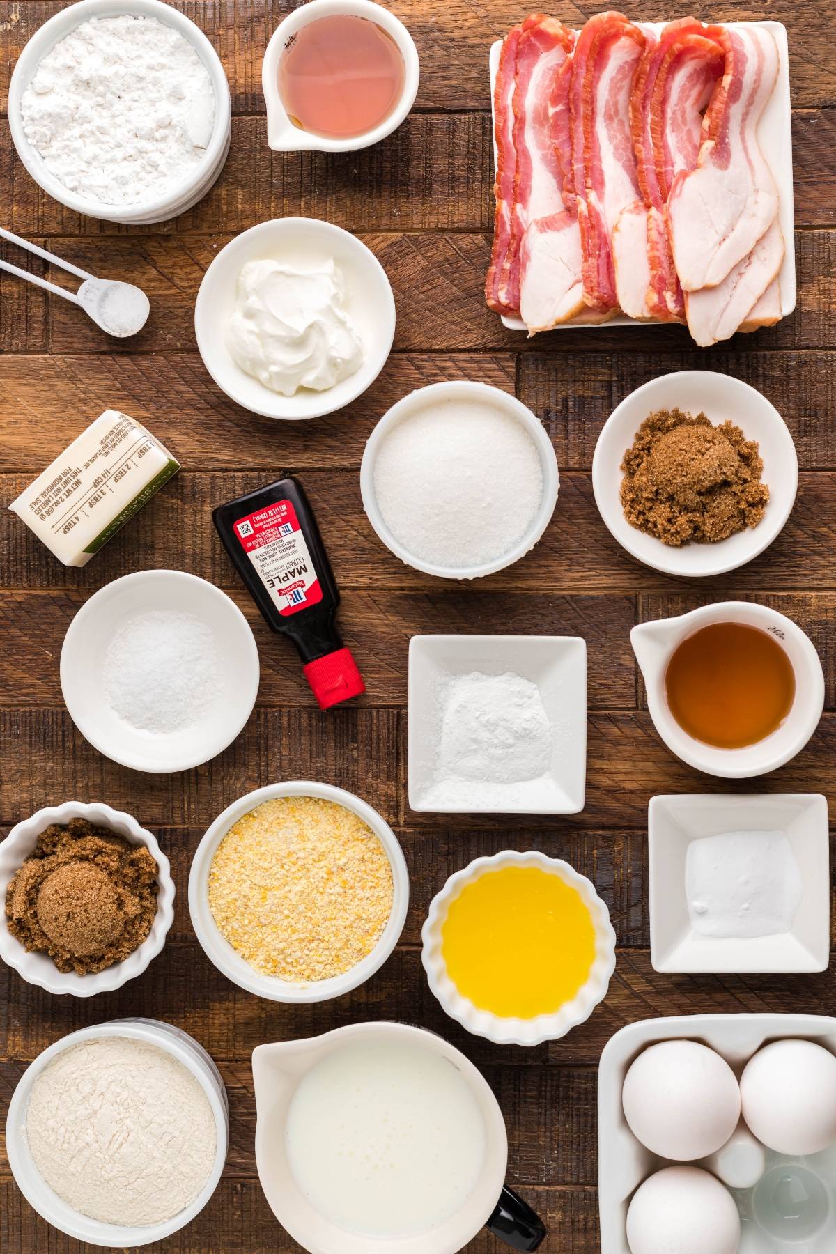 Assorted baking ingredients and bacon slices arranged in bowls and plates on a wooden surface, perfect for preparing sweet cornbread with icing or trying out your favorite air fryer cornbread recipe.