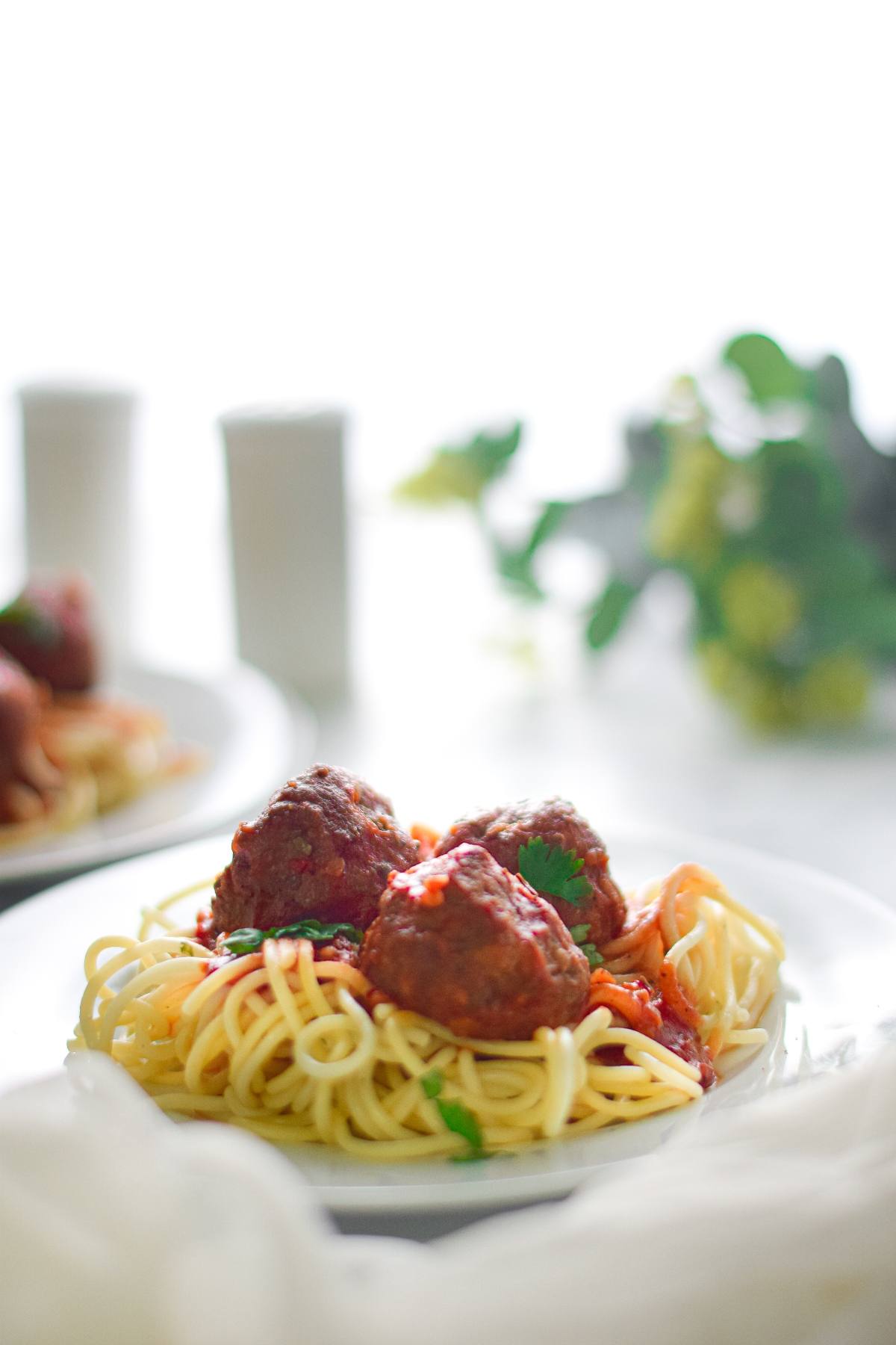 A plate of spaghetti topped with easy vegan meatballs and tomato sauce, garnished with herbs.
