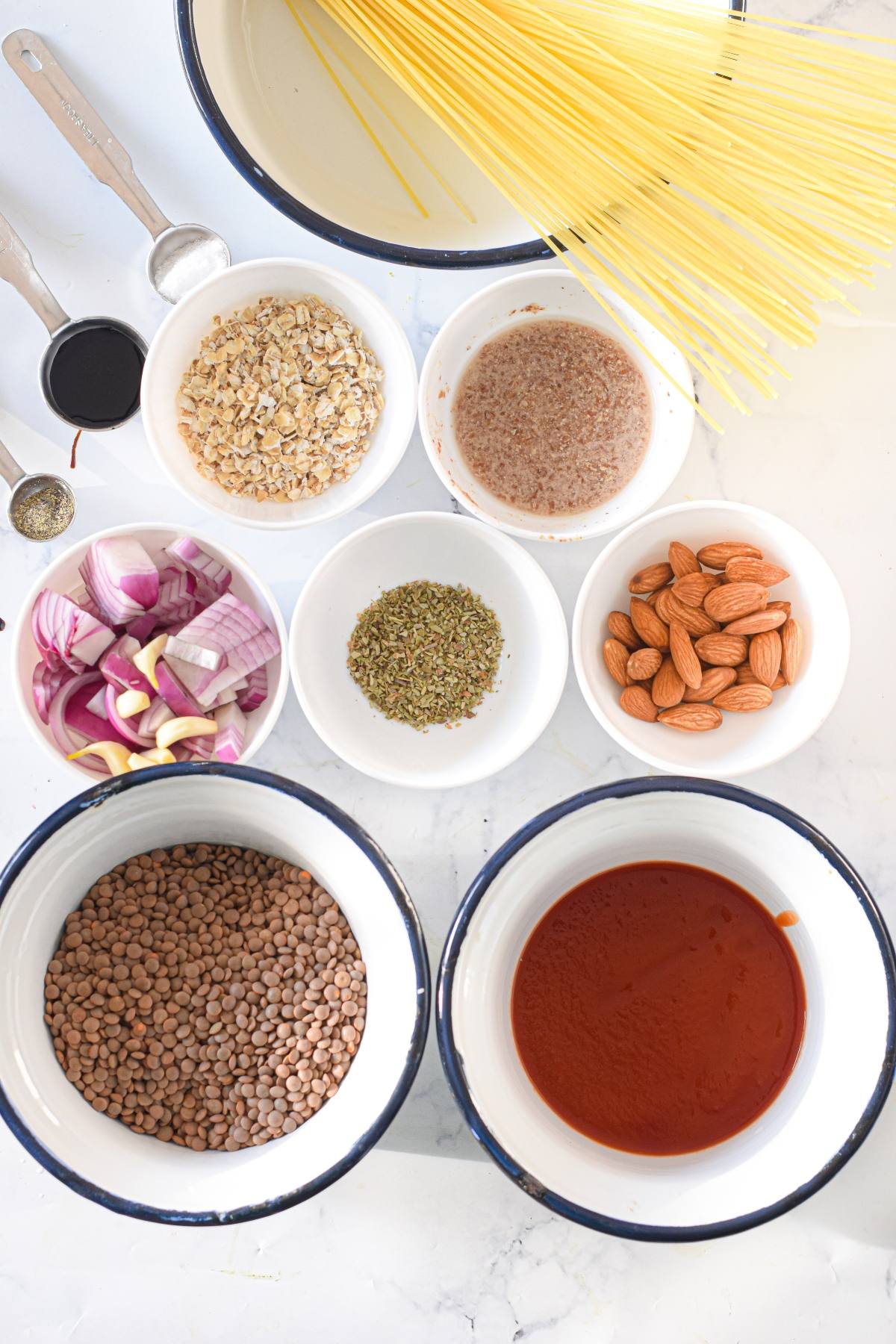 Overhead view of uncooked spaghetti, lentils, tomato sauce, almonds, spices, onions, oats, and measuring spoons—perfect ingredients for a Vegan meatball recipe or Gluten free air fryer meatballs.