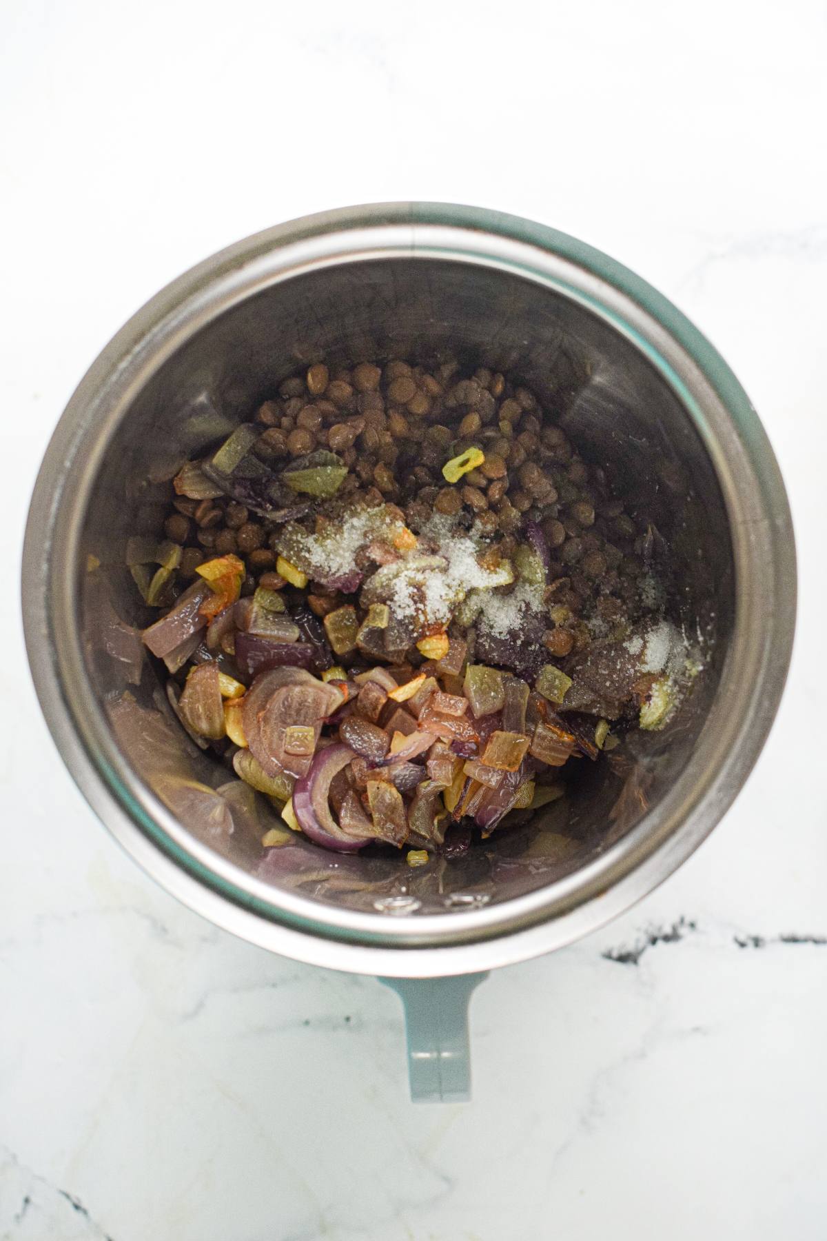 Chopped vegetables and seasonings in a metal pot, ready to be blended for an easy vegan meatball recipe, on a white marble surface.