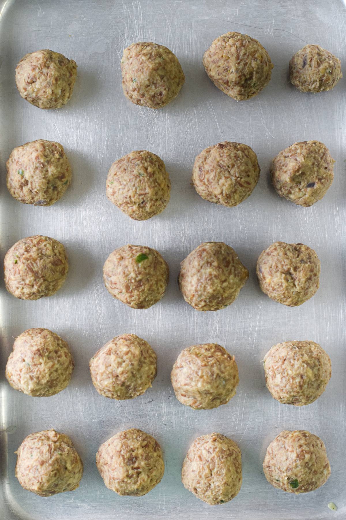 Unbaked easy vegan meatballs arranged in neat rows on a metal baking sheet, ready to be cooked and enjoyed with spaghetti marinara.