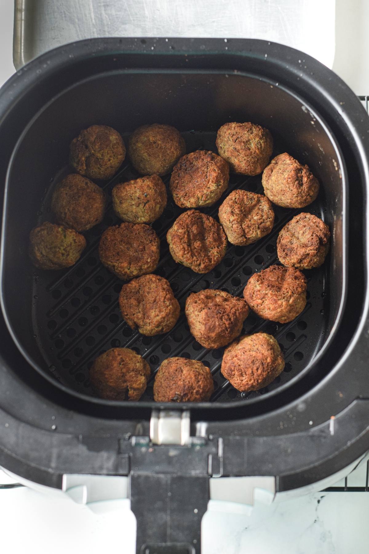Air fryer basket filled with golden-brown falafel balls, similar to gluten free air fryer meatballs, perfectly arranged on the perforated tray.