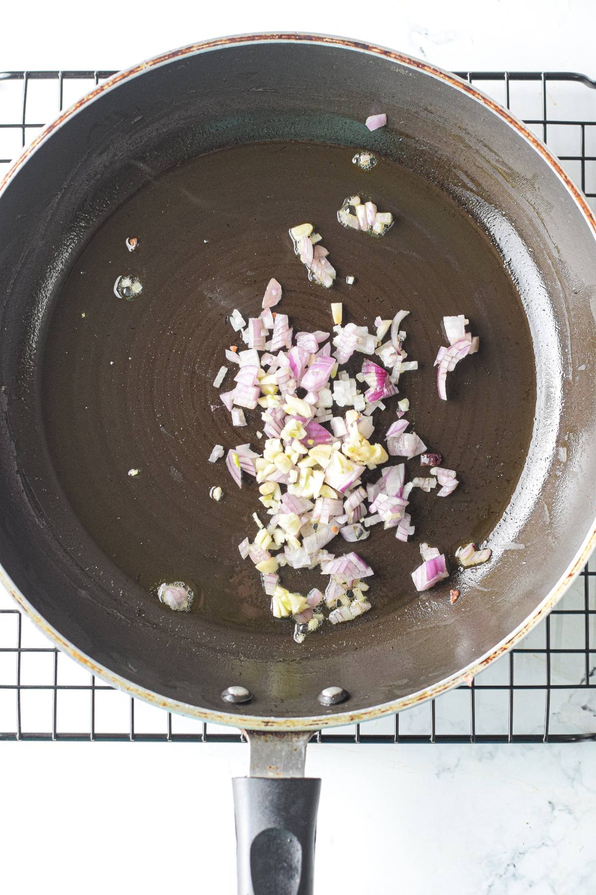Chopped onions and garlic sautéing in a black frying pan on a wire rack, perfect as the aromatic base for gluten free air fryer meatballs.