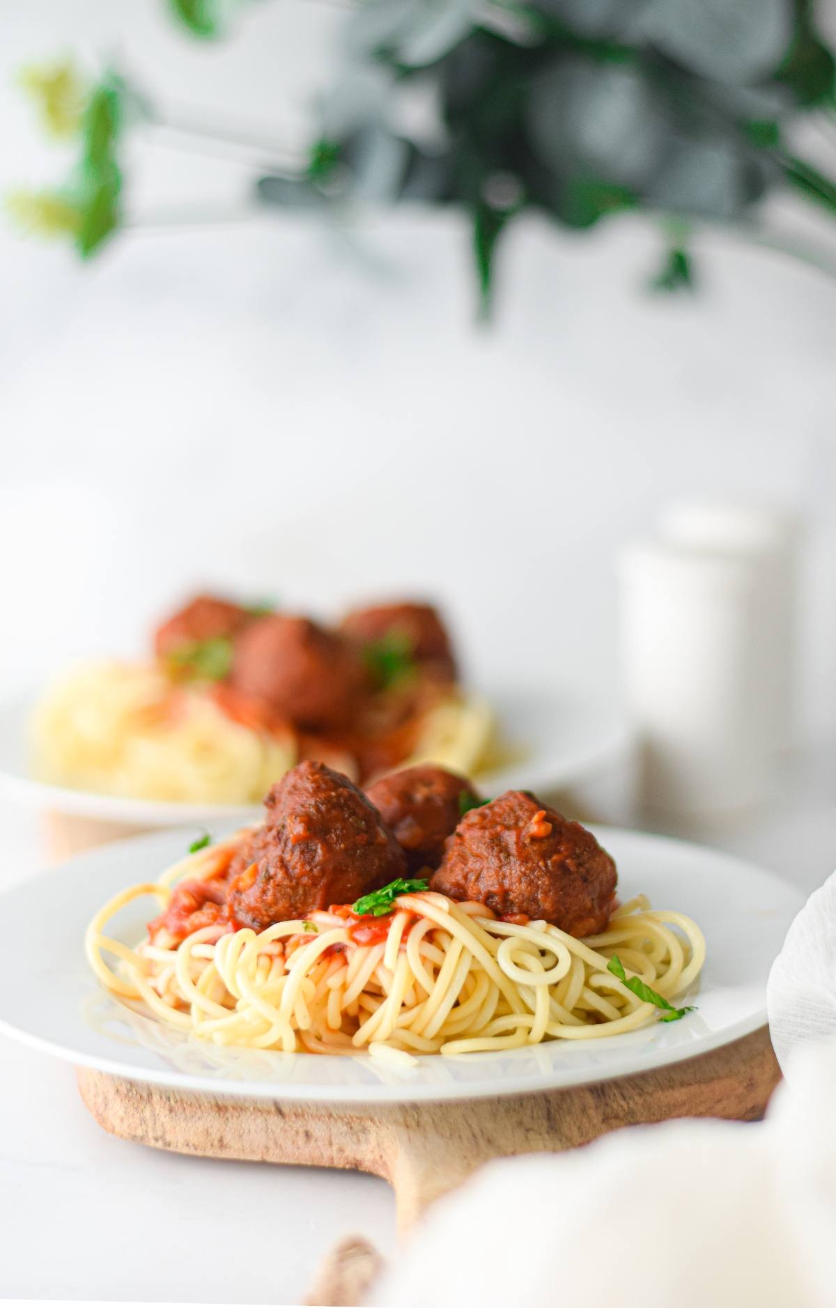 Spaghetti with vegan meatballs in rich marinara sauce served on a white plate, garnished with fresh herbs.