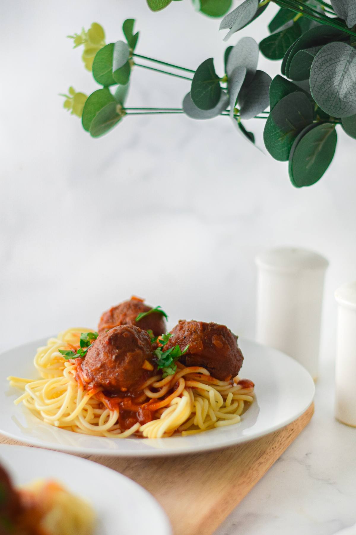 A plate of spaghetti with Gluten Free Air Fryer Meatballs in tomato sauce, garnished with parsley, served on a wooden board.