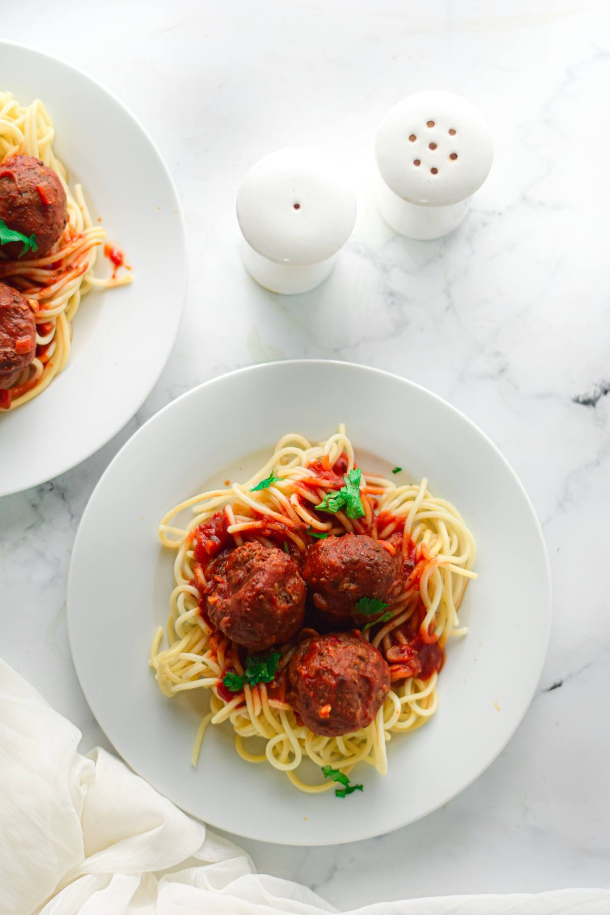 A plate of easy vegan meatballs with spaghetti marinara and parsley, served beside salt and pepper shakers.