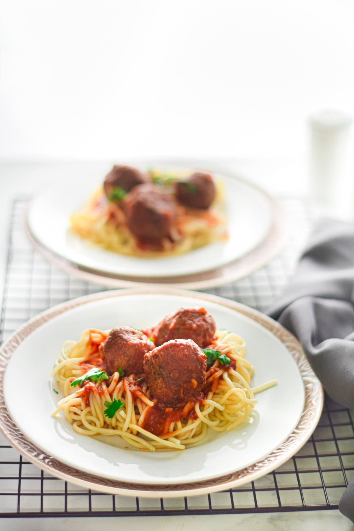 A plate of spaghetti with tomato sauce and easy vegan meatballs, garnished with parsley, sits on a table.