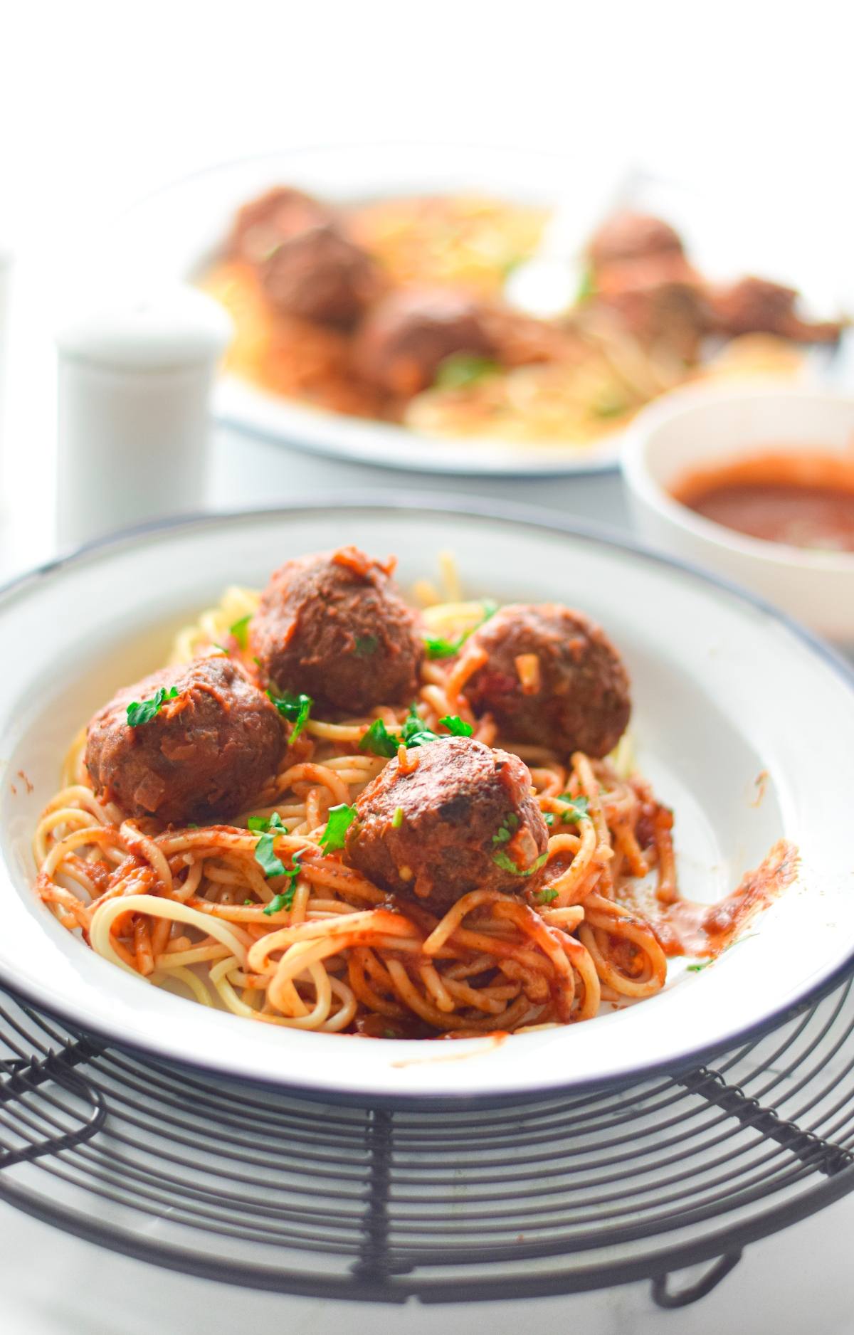 A plate of spaghetti with tomato sauce and vegan meatballs with spaghetti marinara, garnished with parsley, on a wire rack.