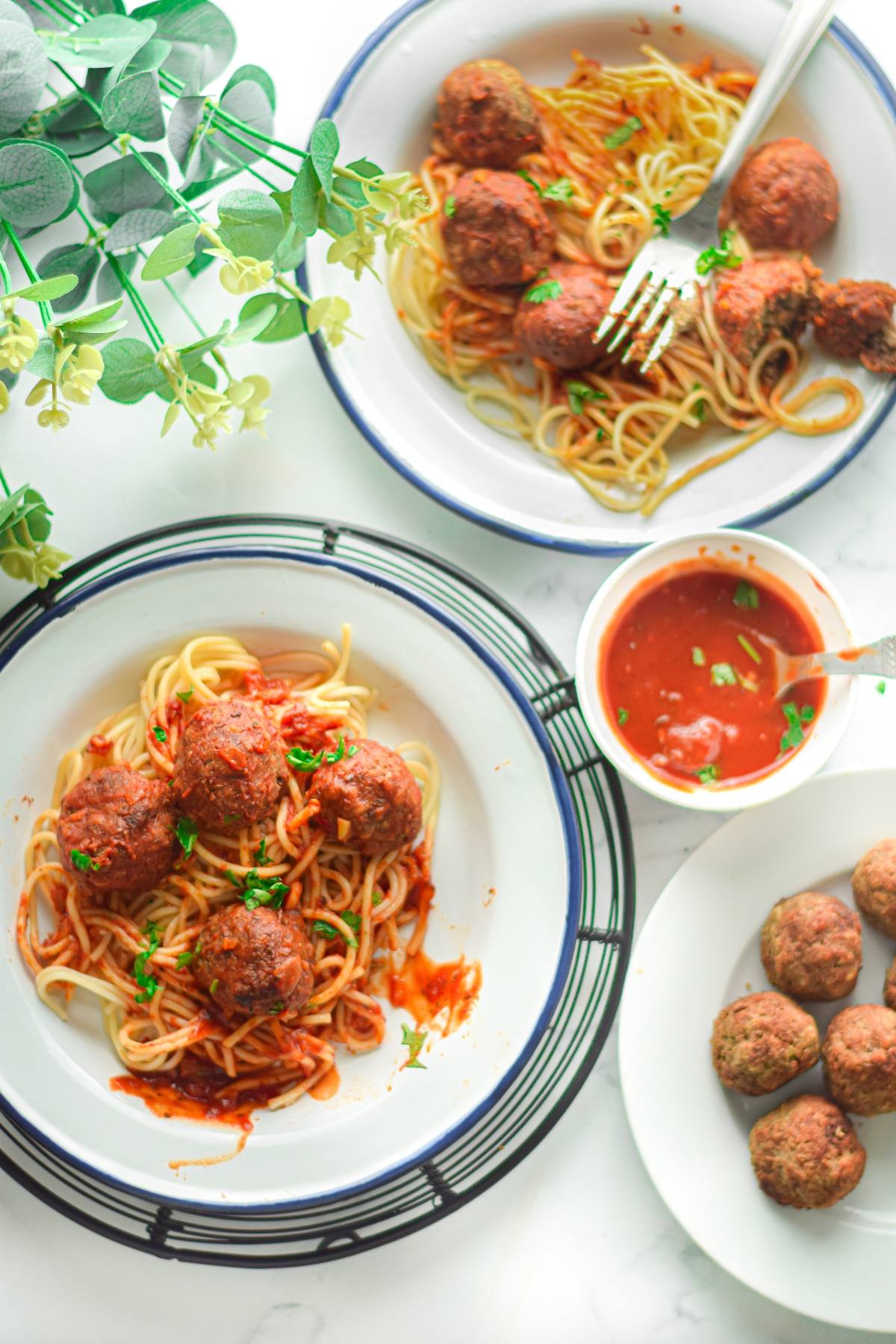 Two plates of vegan meatballs with spaghetti marinara, a bowl of sauce, and a plate of plain vegan meatballs create a delicious plant-based feast.