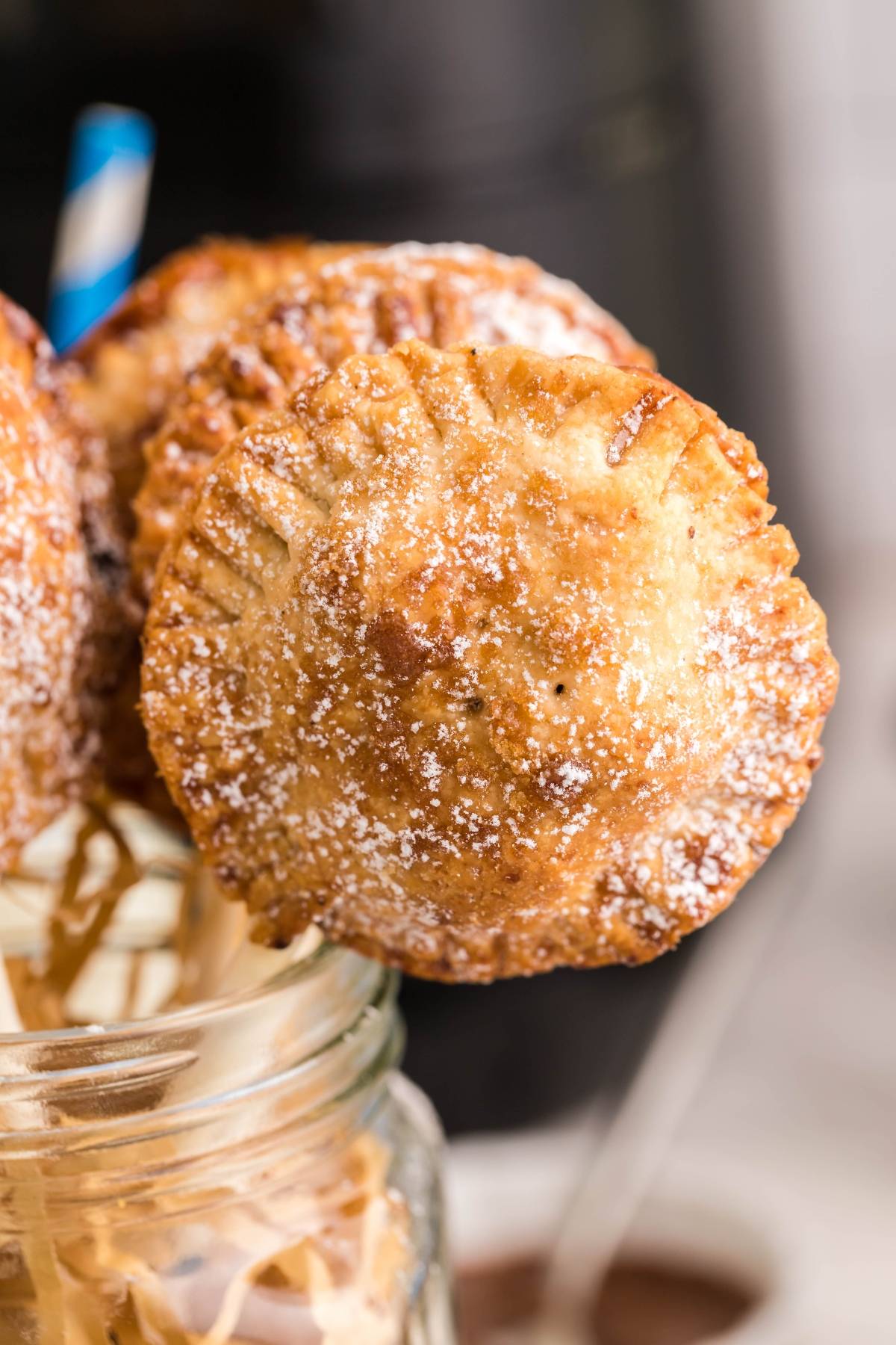 Close-up of golden-brown air fryer s’more pie pops dusted with powdered sugar, displayed in a glass jar—a perfect summer BBQ dessert idea.