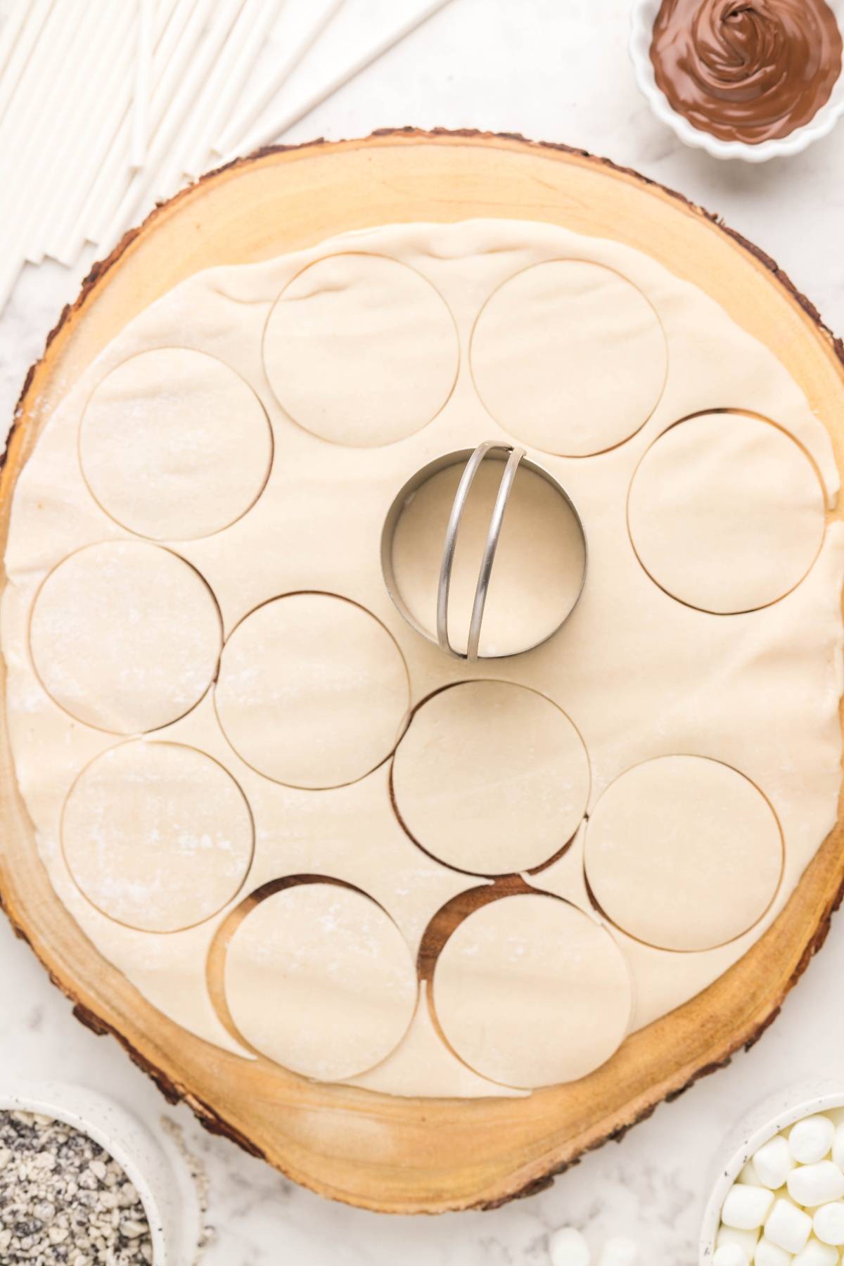 Round dough circles are cut out on a wooden board with a circular cookie cutter in the center—perfect for an easy s’more treats or your next summer BBQ dessert idea.