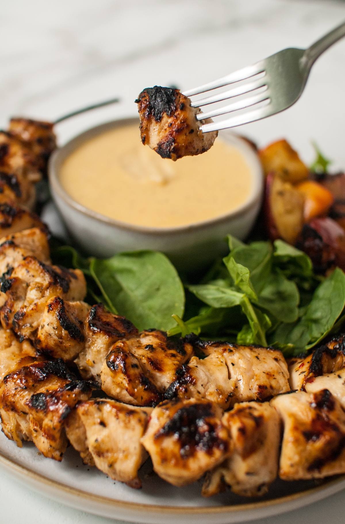 Cider grilled chicken skewers with greens and dipping sauce, with a fork lifting a tender piece above the plate.