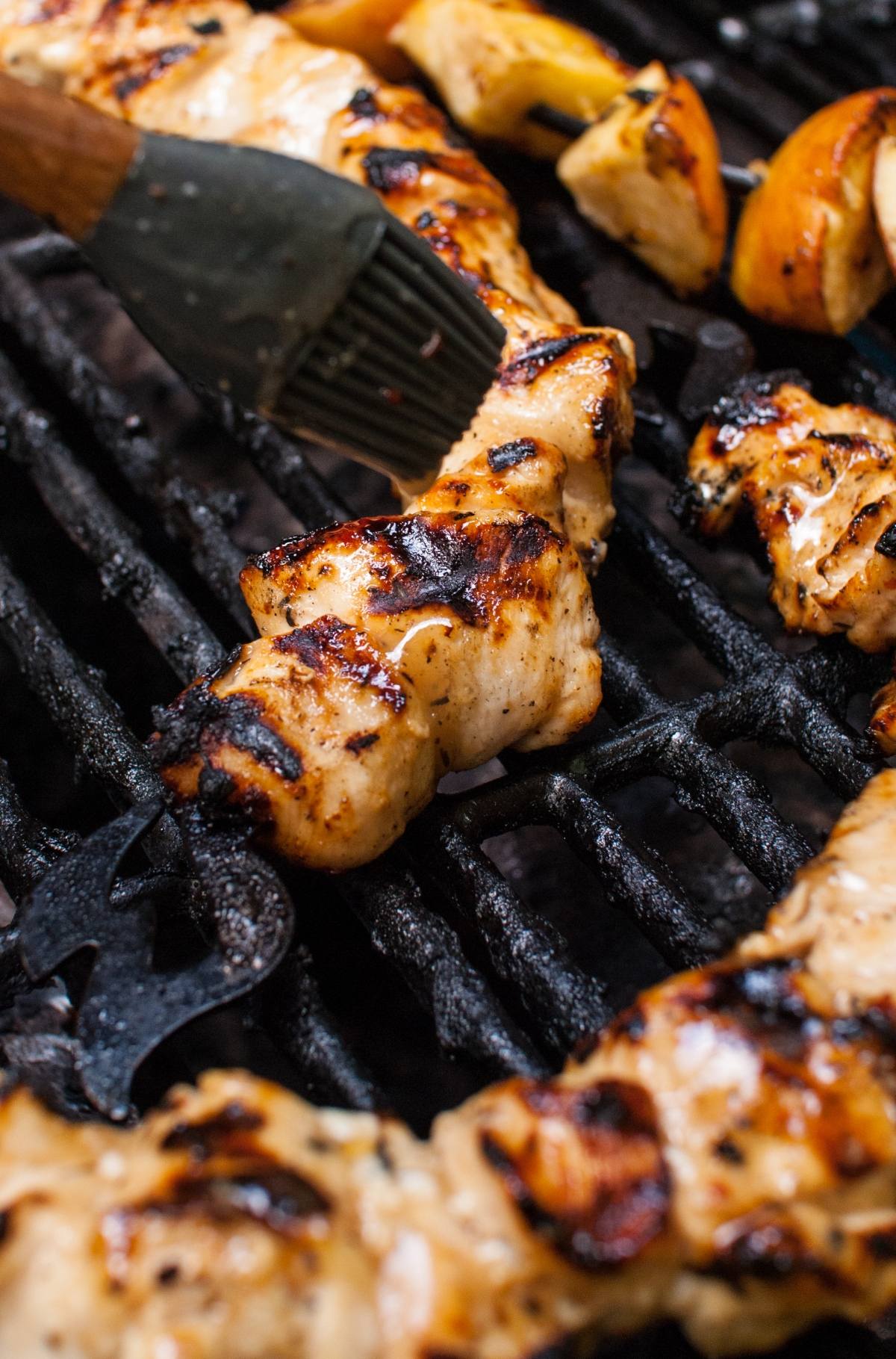 Apple Cider Chicken Skewers with Gouda Sauce are brushed with marinade as they grill on the barbecue, boasting delicious charred marks.