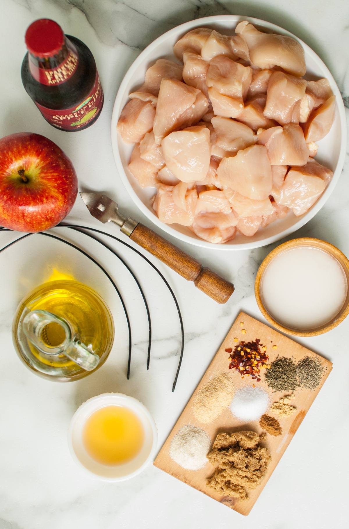 Raw cubed chicken, apple, apple cider, spices, oil, soy sauce, and sugar arranged on a marble surface—perfect ingredients for Apple Cider Chicken Skewers with Gouda Sauce or a flavorful apple cider chicken marinade.