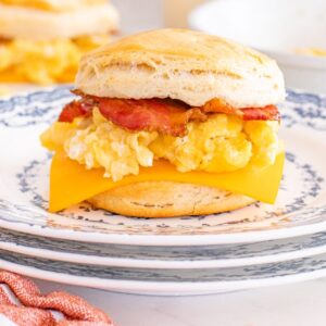 Savor our biscuit breakfast sandwiches, featuring bacon, scrambled eggs, and cheddar cheese on a warm biscuit, served on a patterned plate.