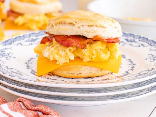 Savor our biscuit breakfast sandwiches, featuring bacon, scrambled eggs, and cheddar cheese on a warm biscuit, served on a patterned plate.