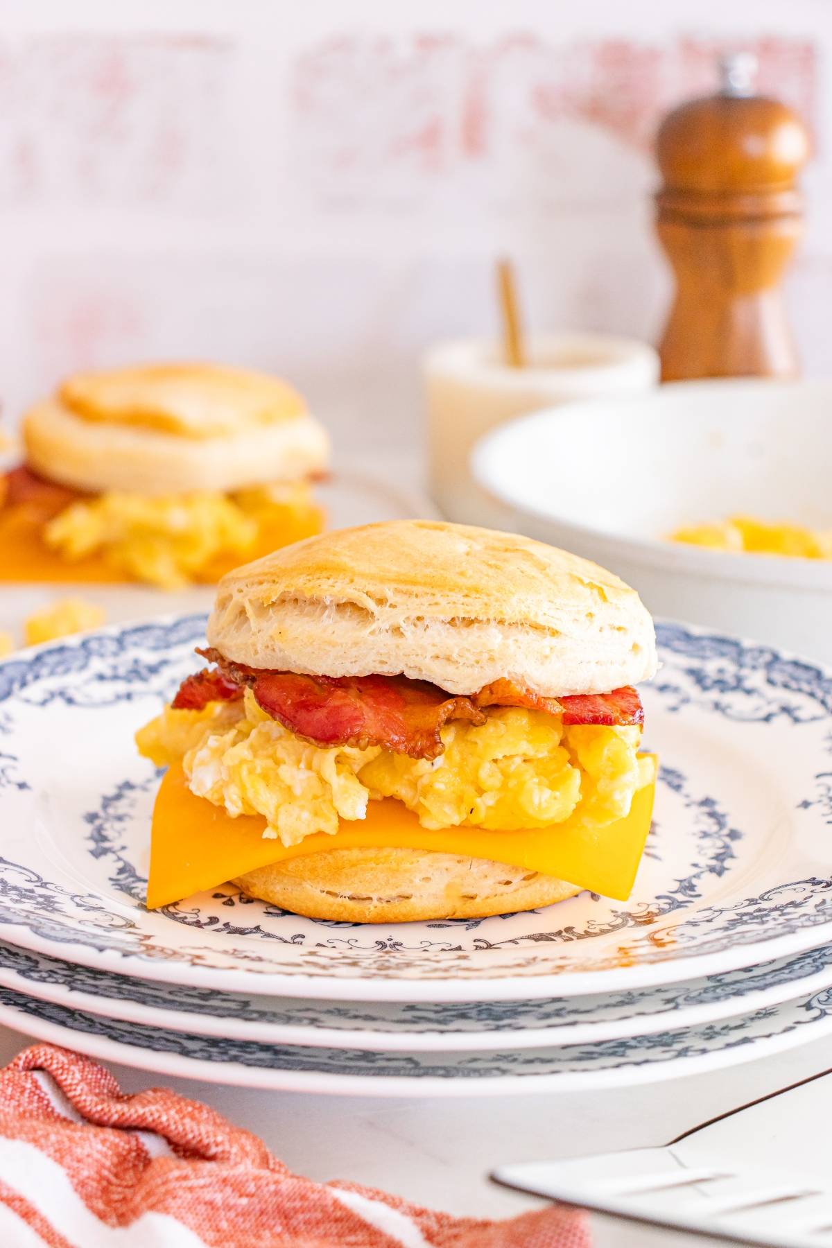 Breakfast sandwich with egg, bacon, and cheese on a biscuit, served on a patterned plate.