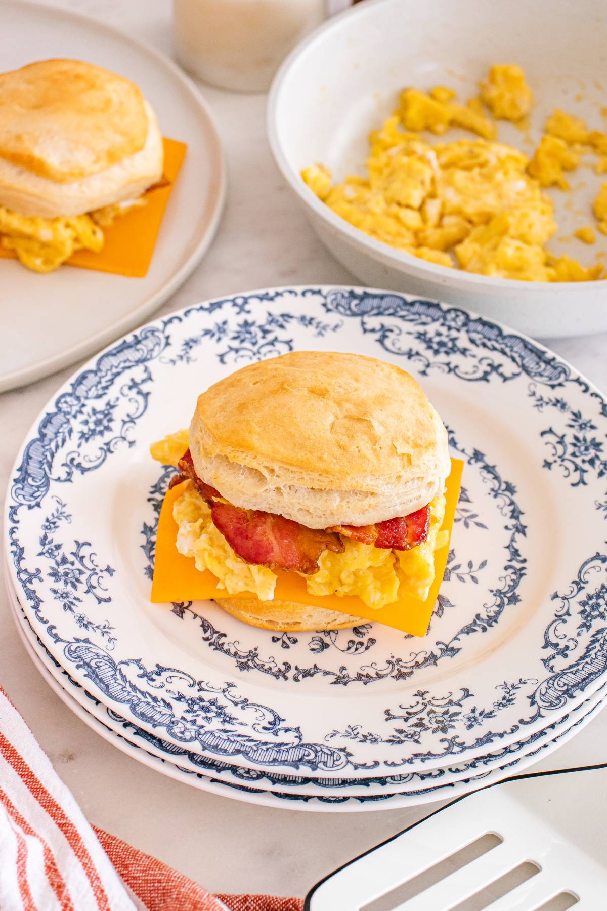A breakfast sandwich with egg, bacon, and cheese on a biscuit, served on a blue and white plate.