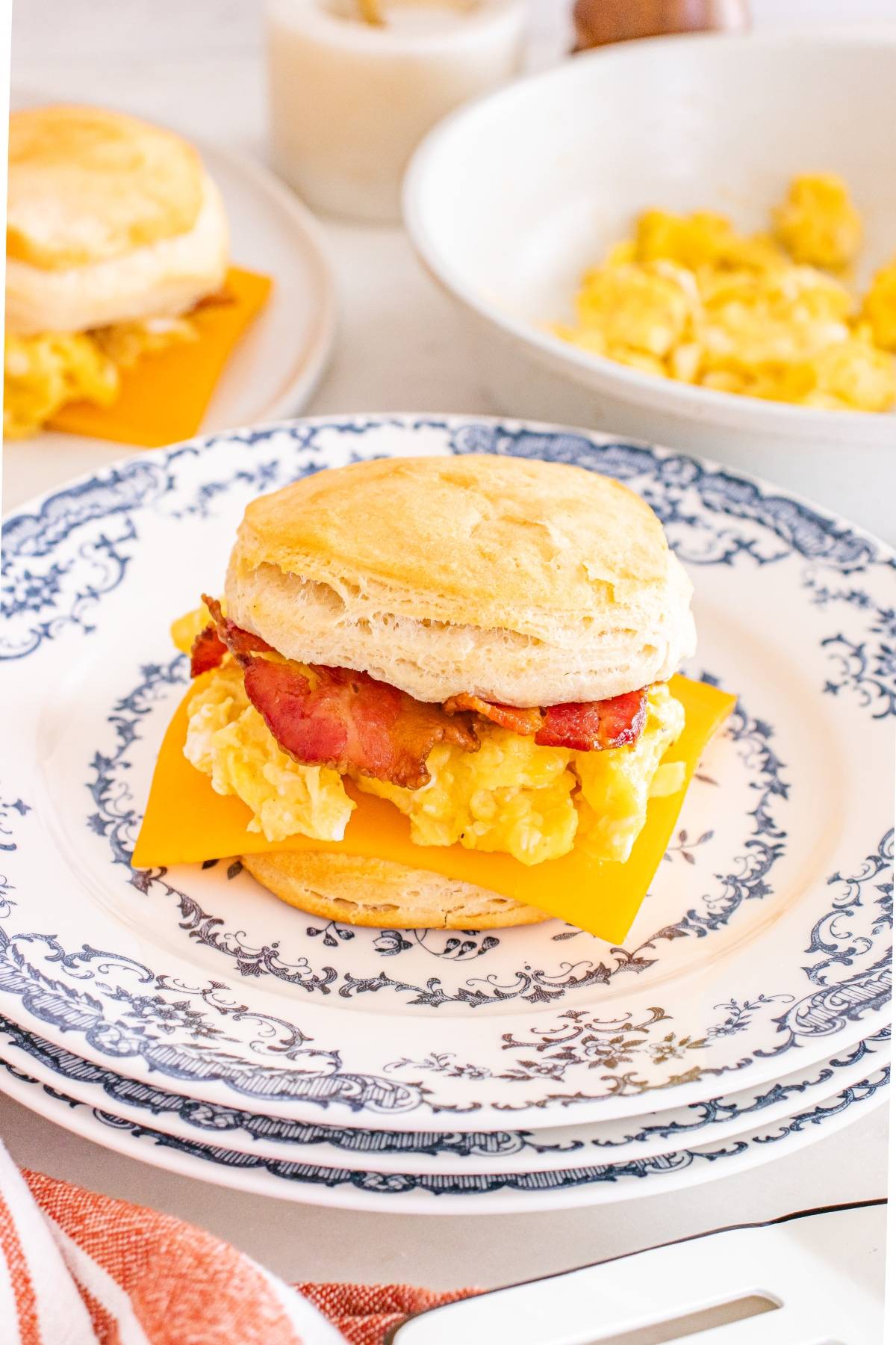 A breakfast sandwich with egg, bacon, and cheddar cheese on a biscuit, served on a decorative plate.