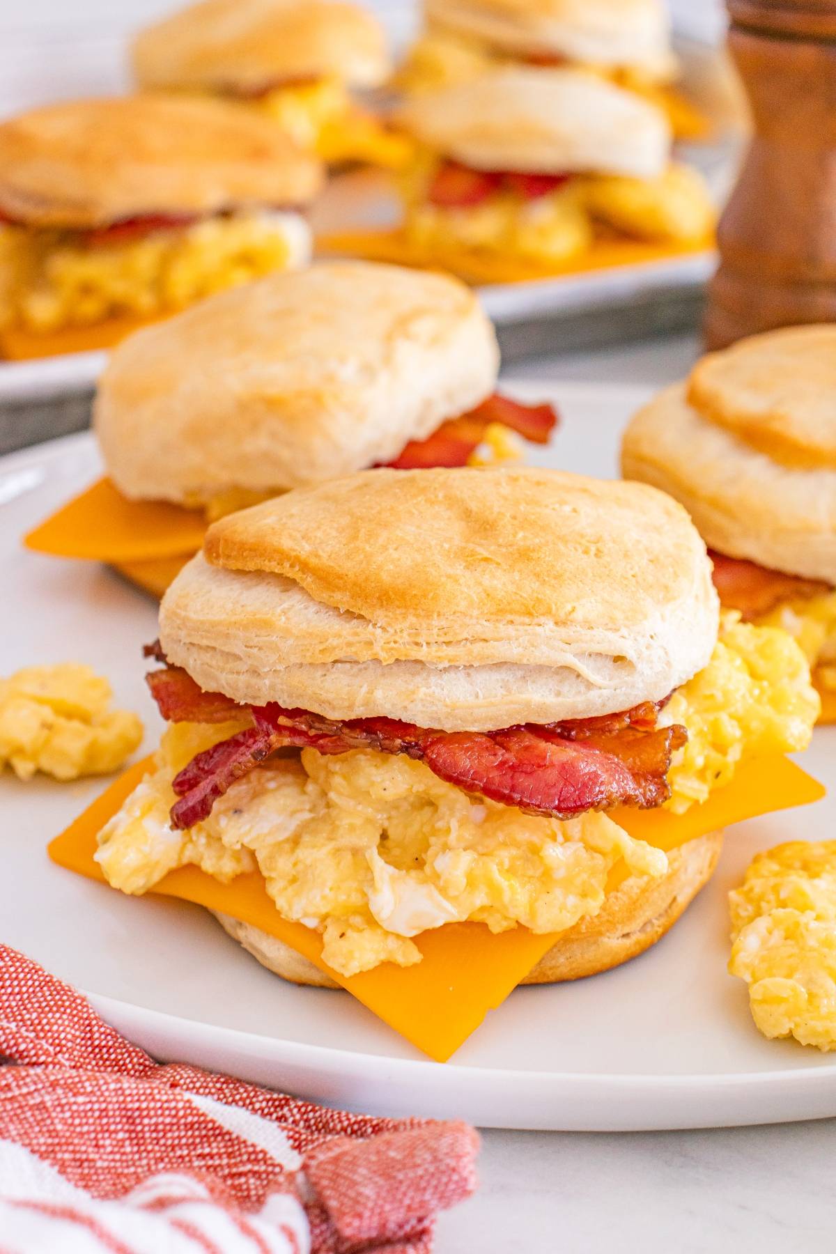 Breakfast sandwiches with scrambled eggs, cheddar cheese, and bacon on biscuits, served on a white plate.