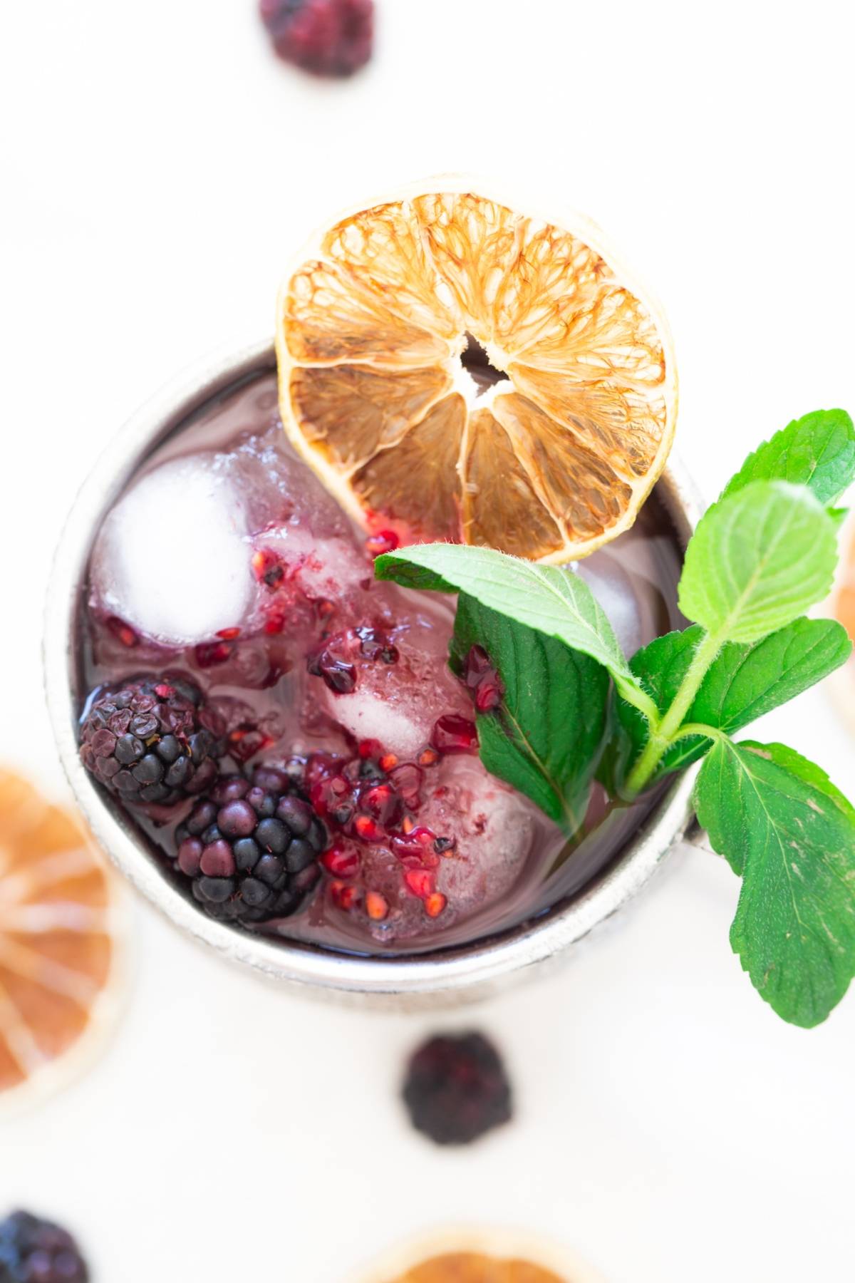 A refreshing cocktail with vodka featuring ice, blackberries, mint, and a dried orange slice garnish, viewed from above—perfect if you’re looking for a fruity recipe with ginger beer.